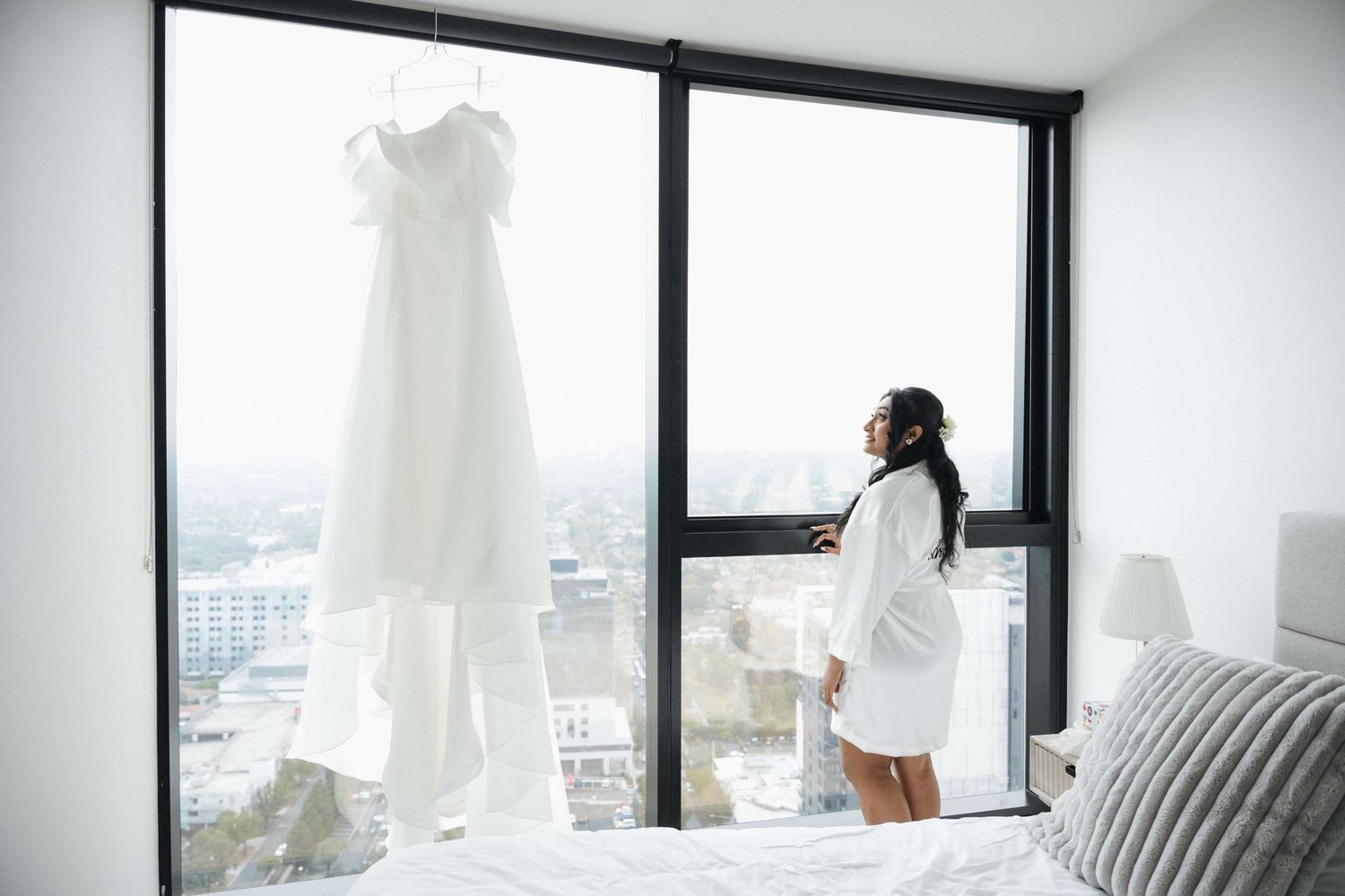 White wedding dress displayed in modern room with large windows and city views.