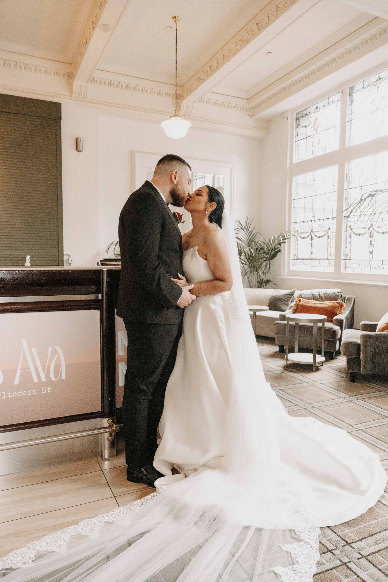 Bride and groom share a romantic kiss in an elegant venue, bride wearing a flowing white gown with long veil.