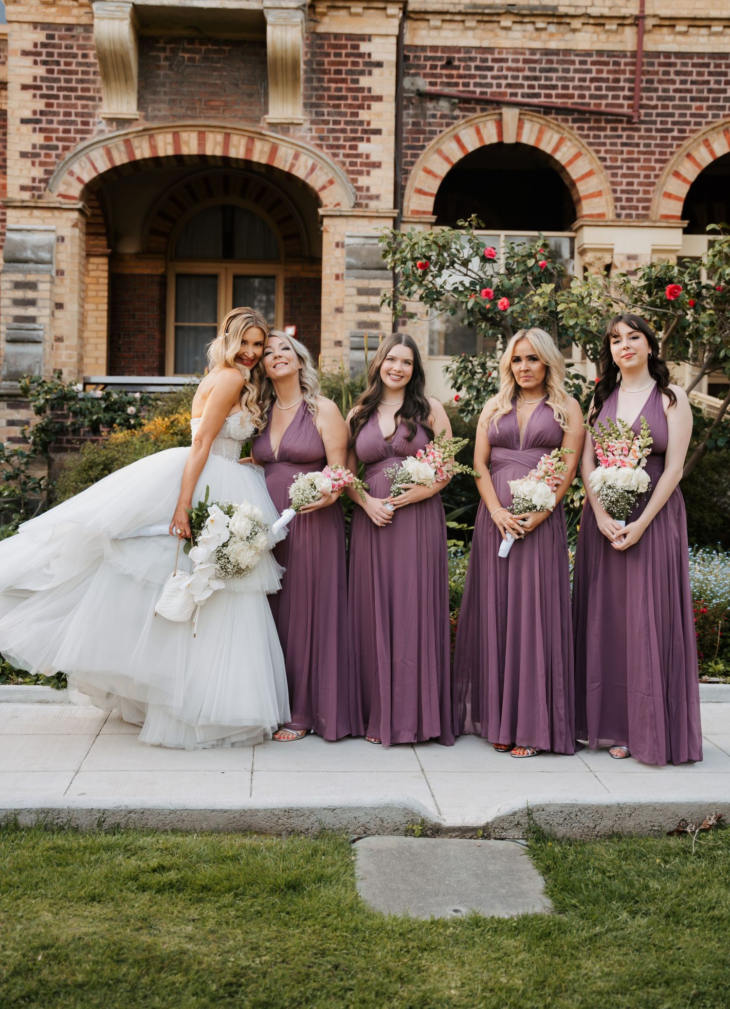 Wedding party in mauve bridesmaid dresses pose together in a candid series of outdoor photos at a brick venue.