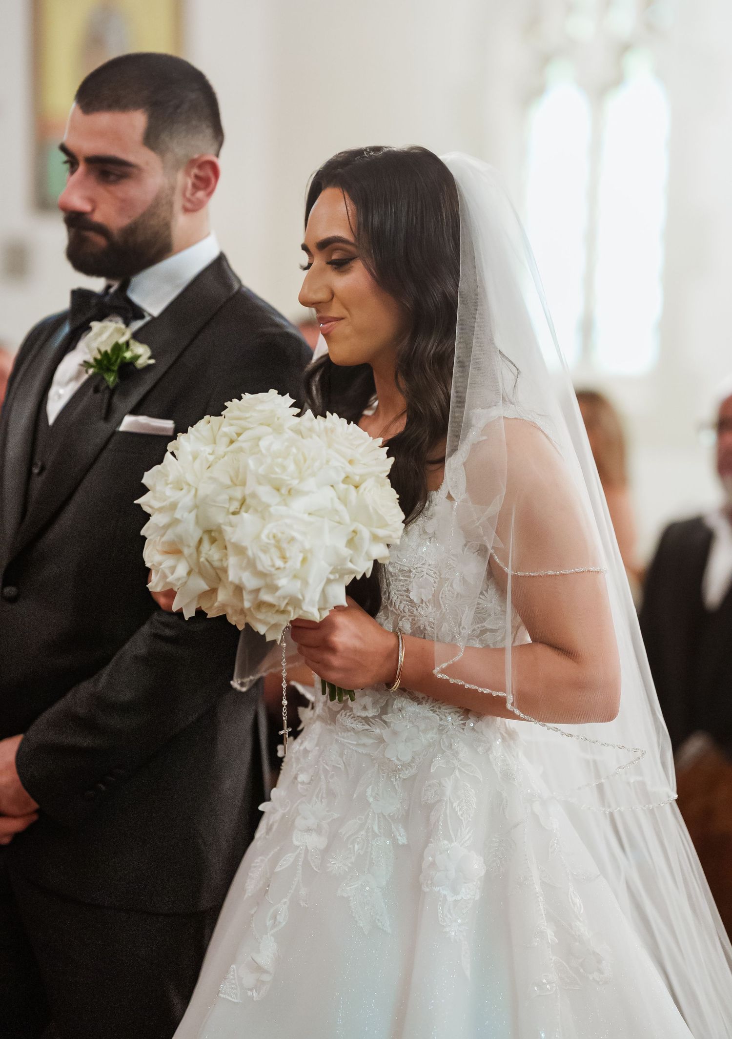 Newlyweds at altar in traditional black tuxedo and white wedding dress holding white floral bouquet.