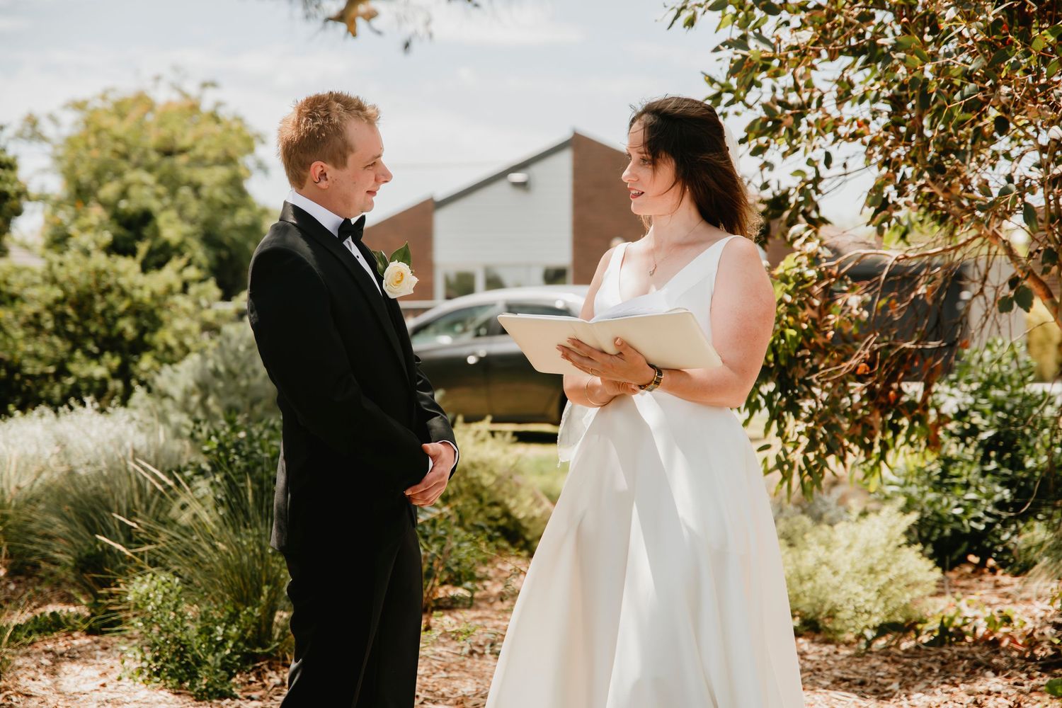 A couple exchanges vows during an outdoor autumn wedding ceremony surrounded by fall foliage.