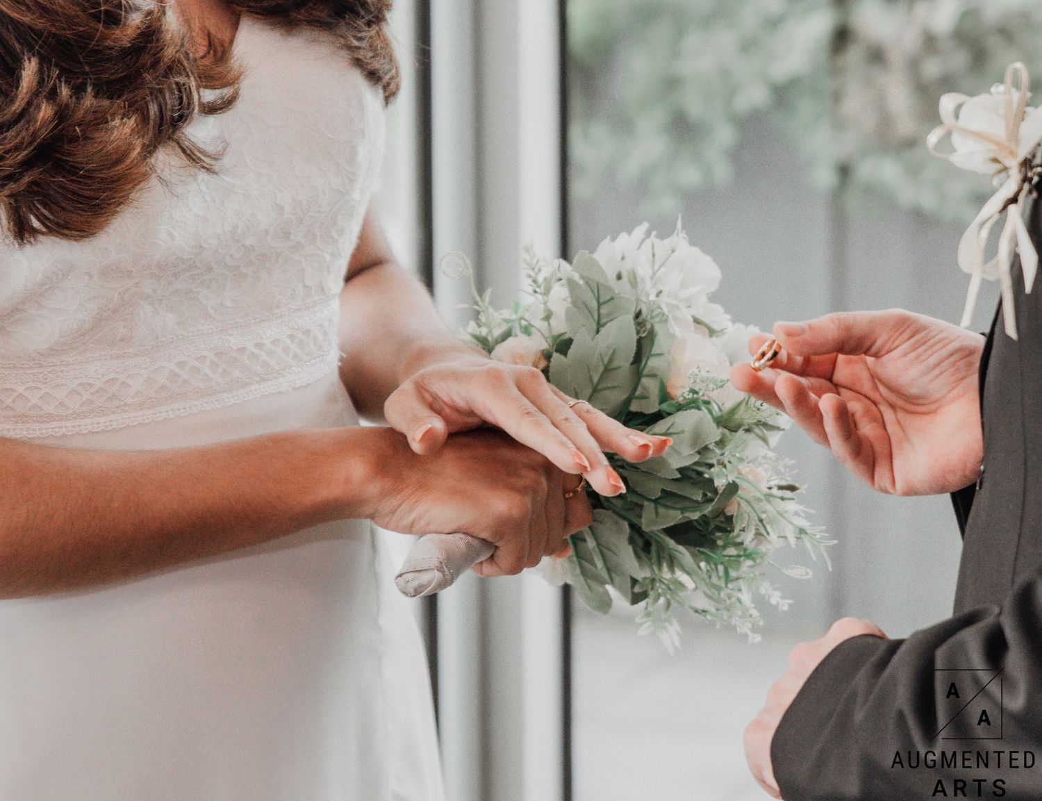 Close-up view of hands holding a delicate white floral bouquet against a soft neutral background.
