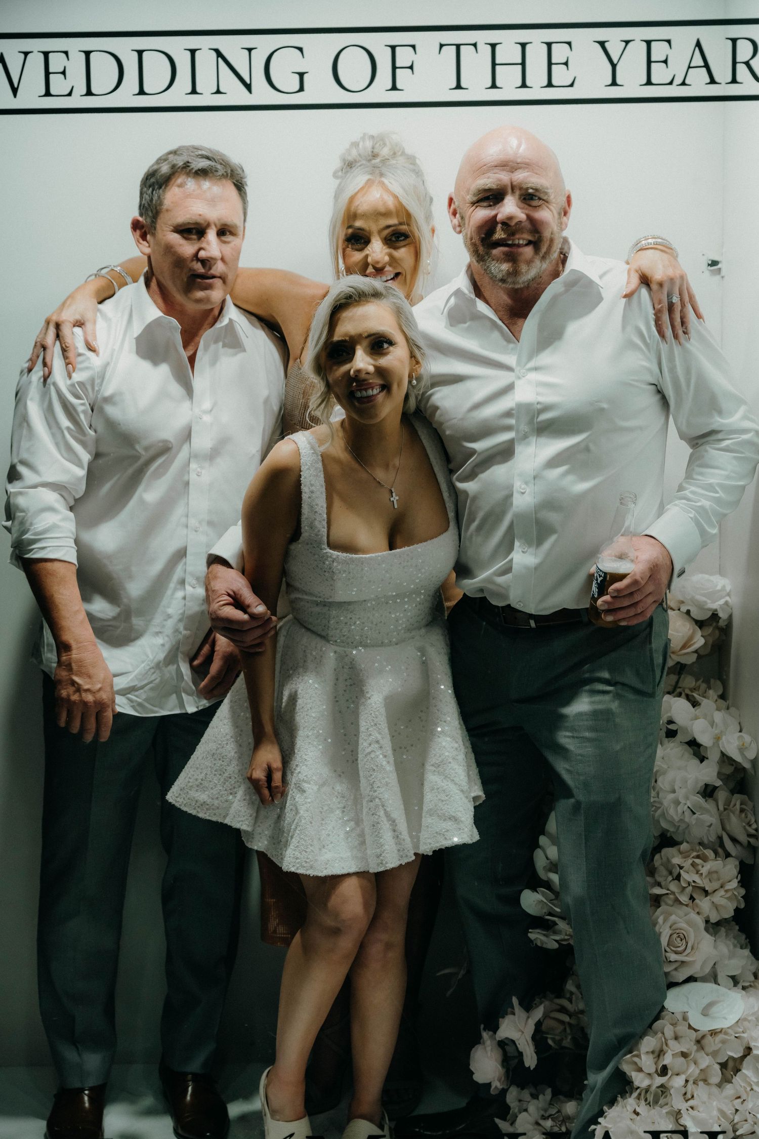 Wedding party poses playfully against a white wall in matching white outfits for a fun photo series.