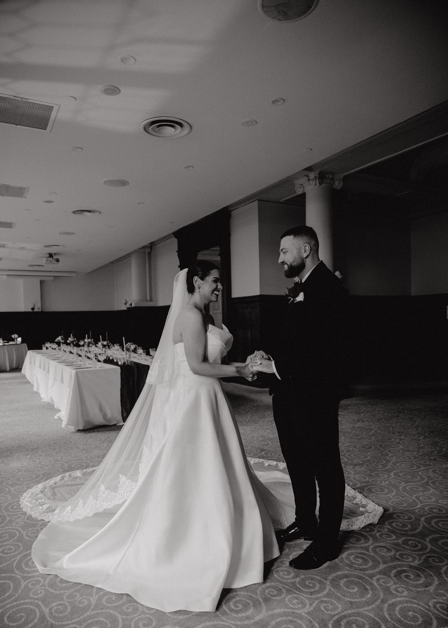 Black and white photo of a bride and groom exchanging vows in an elegant ballroom wedding venue.
