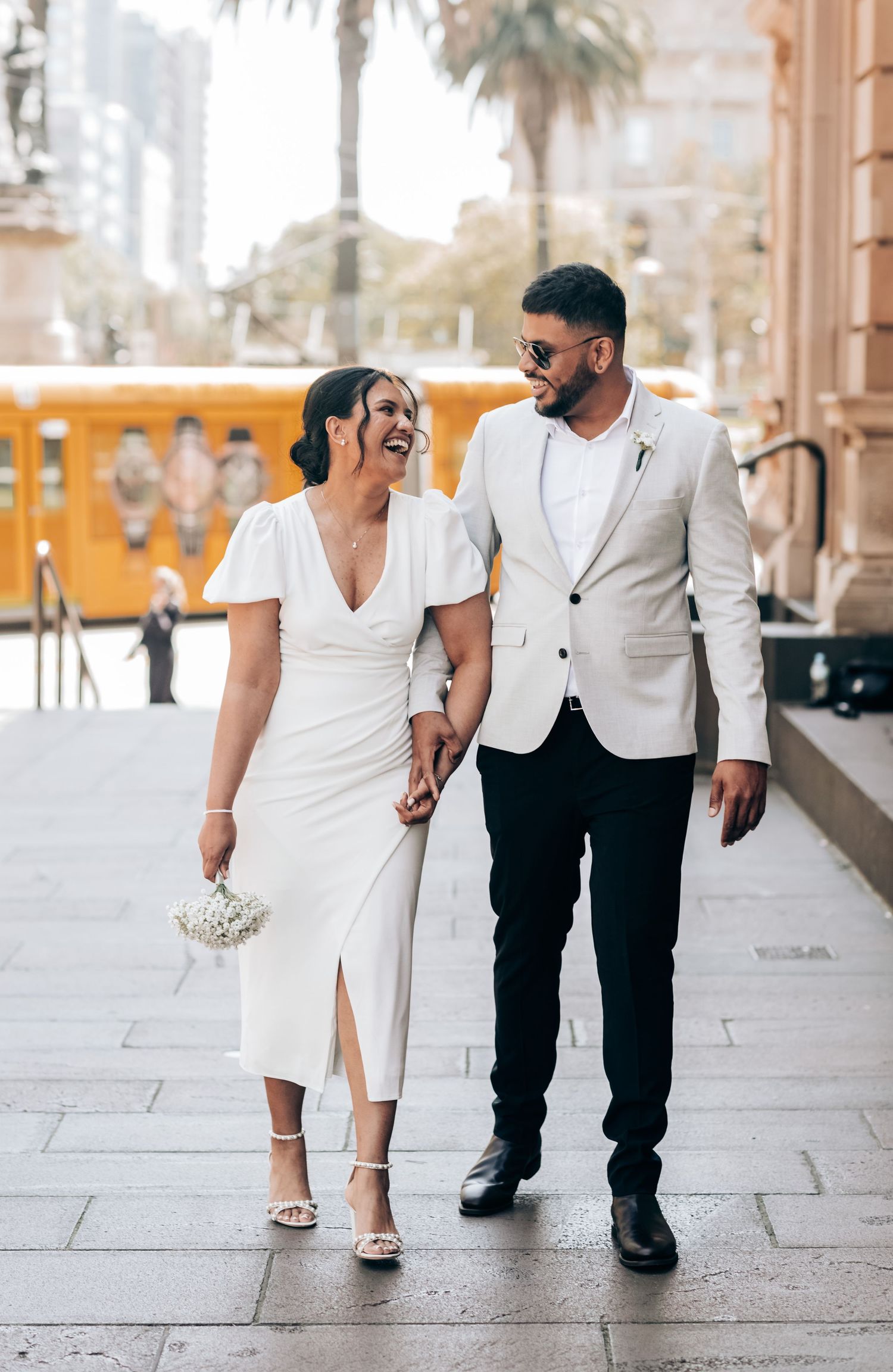 Couple in white and black attire walking together on stone pavement while holding hands in romantic outdoor setting.
