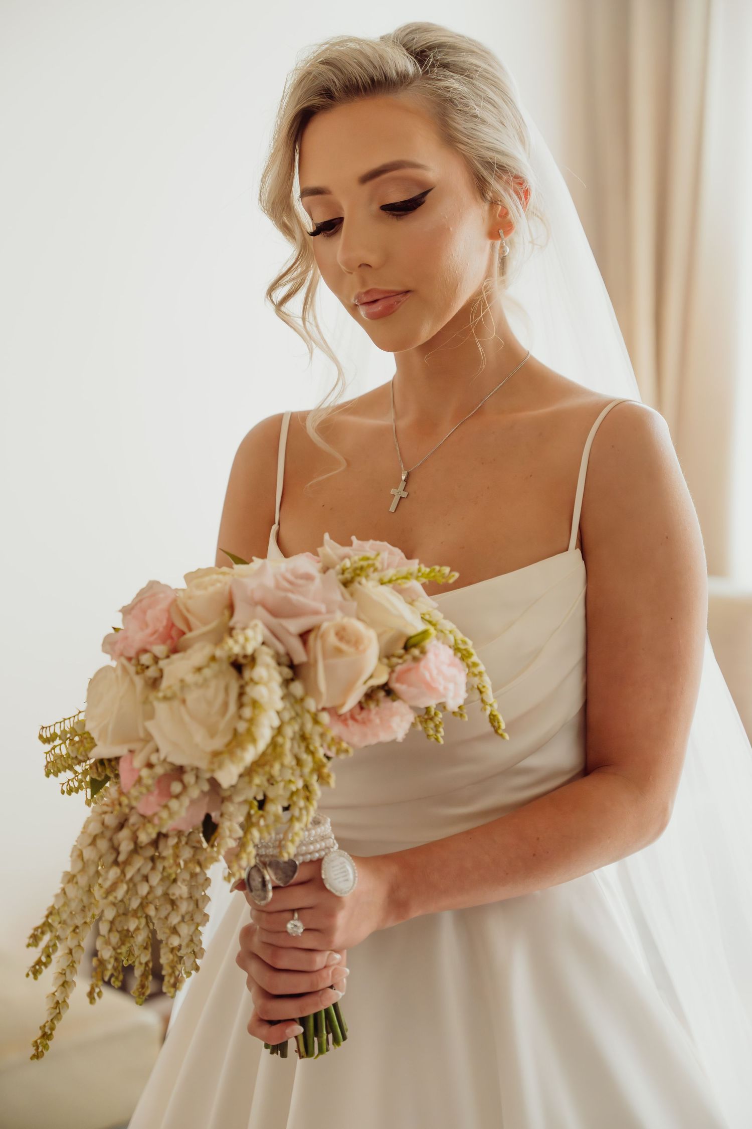 Close-up details of bride holding delicate pink and white wedding bouquet with cascading floral elements.