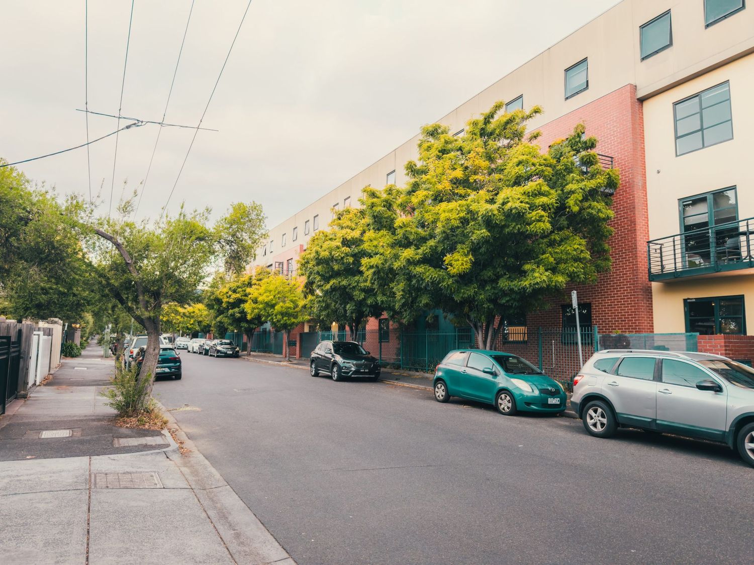 A residential street lined with autumn trees and parked cars next to pink apartment buildings on an overcast day.