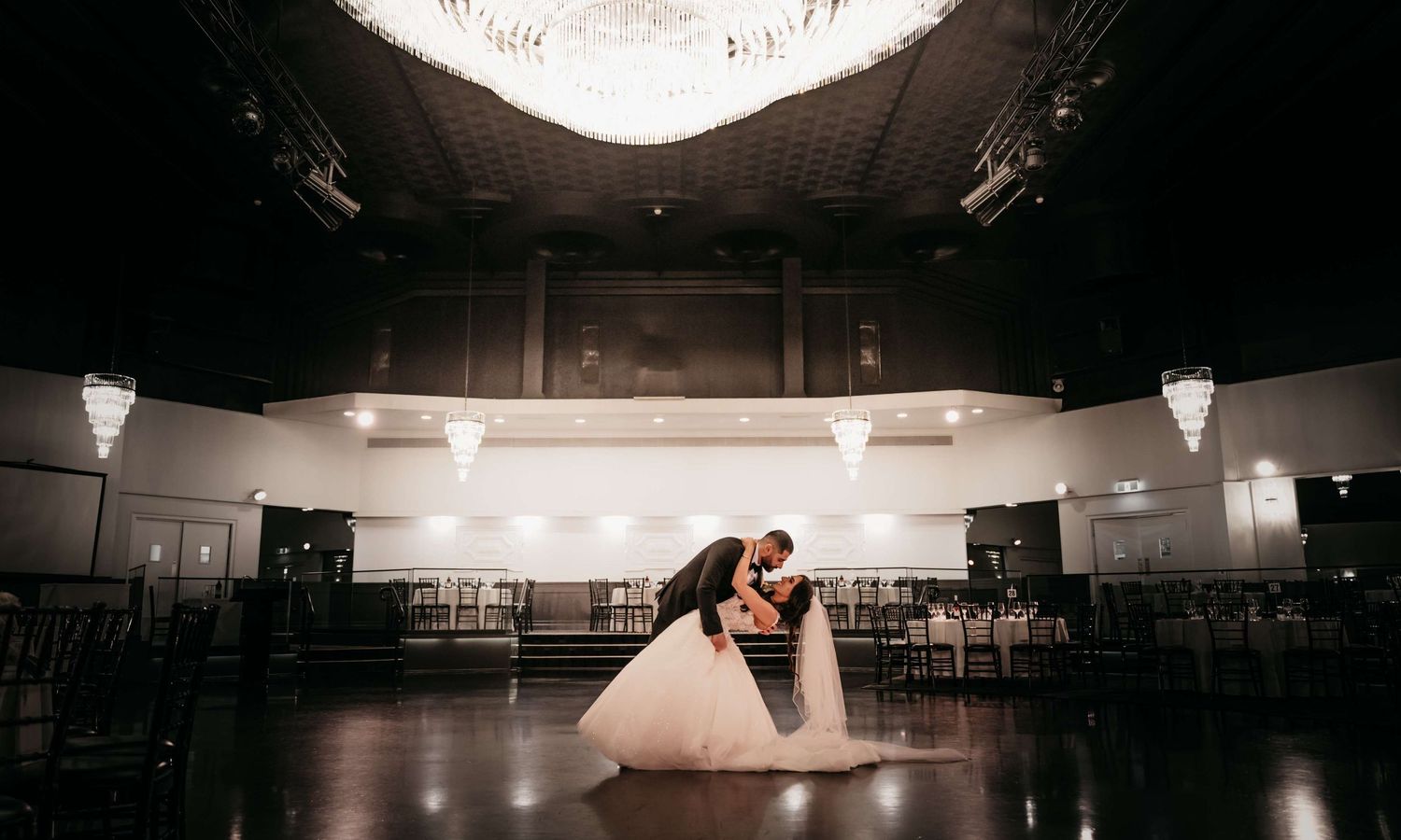 Two silhouettes dance in a romantic embrace on an empty ballroom floor under dramatic lighting.