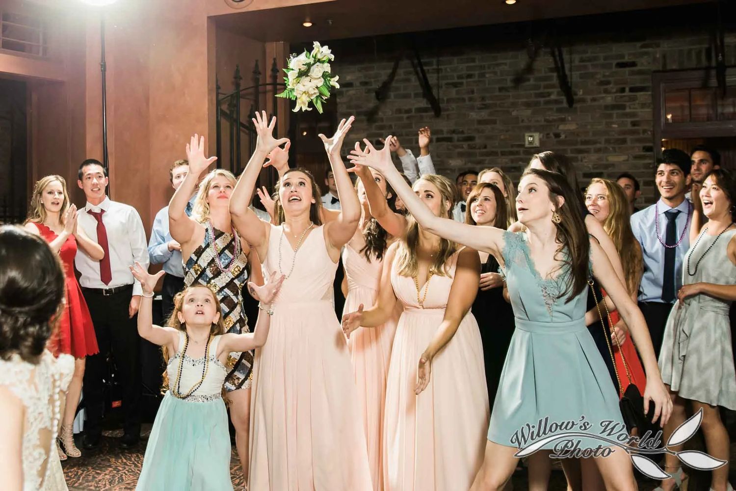 Wedding guests dance together on a dimly lit dance floor at an evening reception celebration.