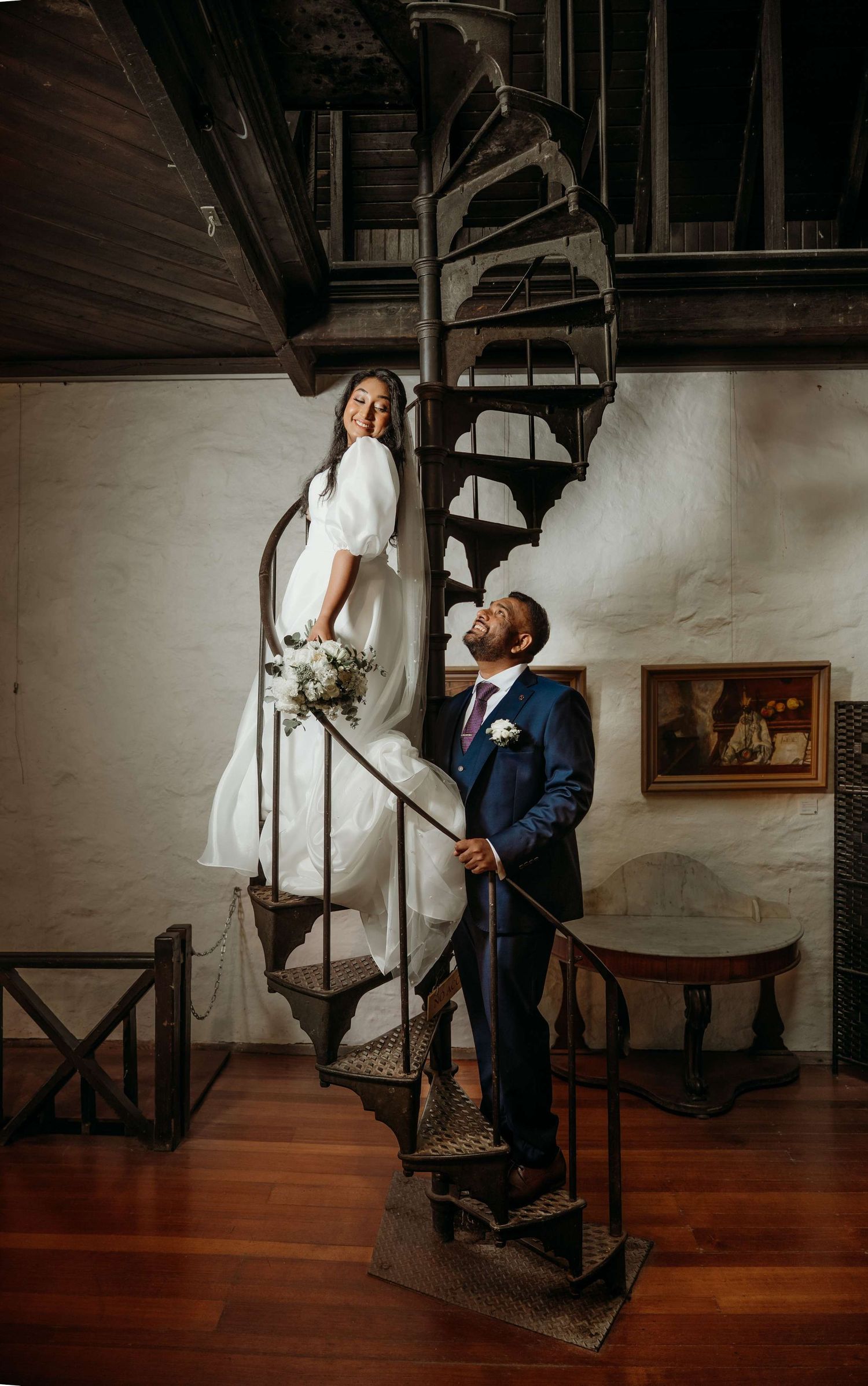 A couple shares an intimate moment on a rustic wooden spiral staircase in low light photography.