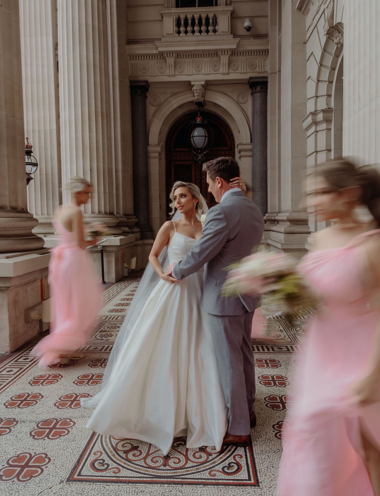 Motion blur panorama of couples dancing in an ornate ballroom with classical columns and decorative floor patterns.