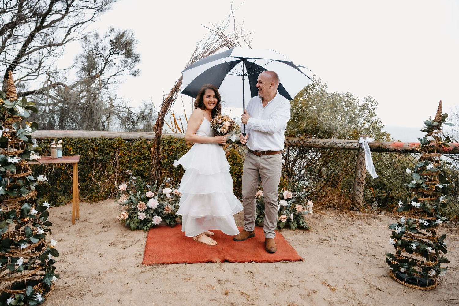Couple on beach swing surrounded by decorated Christmas trees and ocean views during sunset wedding ceremony.