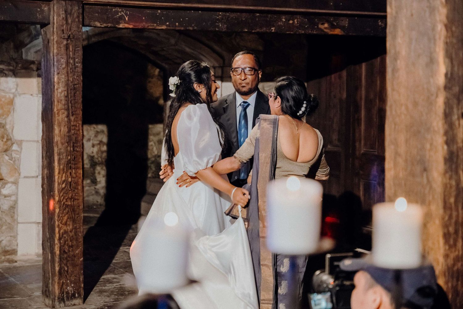 Wedding guests celebrate together in a rustic venue illuminated by candlelight and warm lighting.