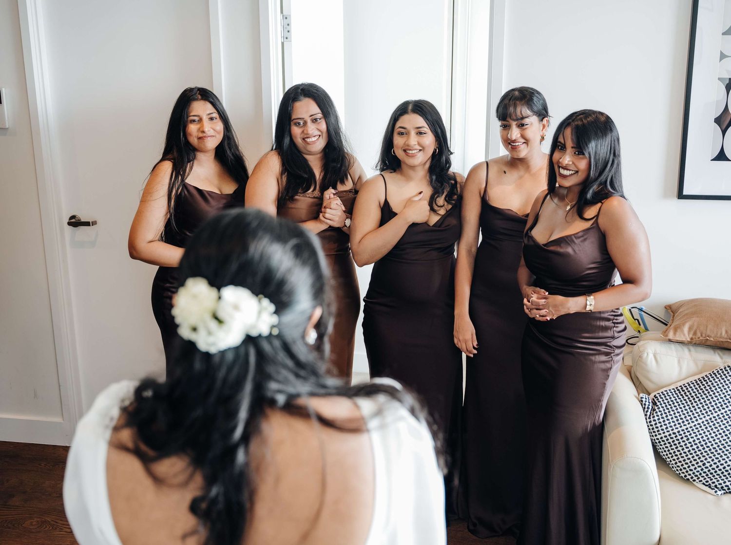 Bridesmaids in matching black dresses gather around and smile during a pre-wedding celebration.