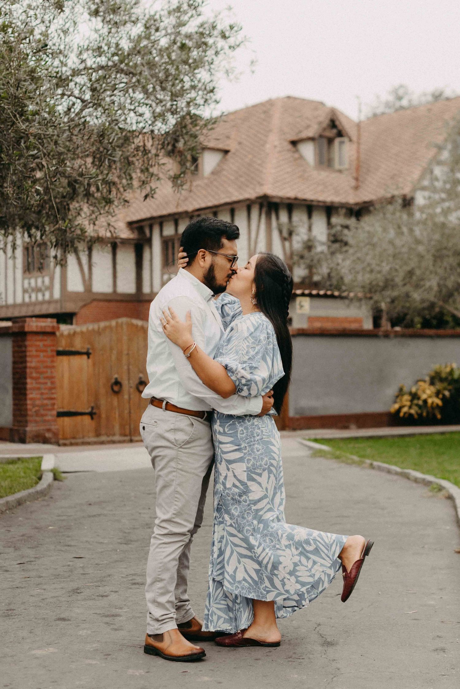 A tender moment shared between a couple outside a Tudor-style house with brick accents.