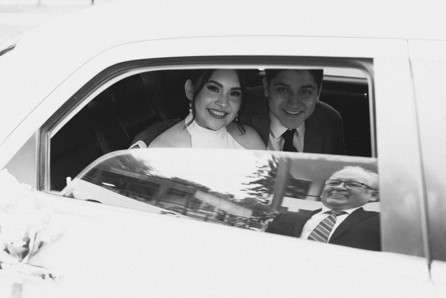 A vintage black and white photo of a happy couple sitting in a car on their wedding day.