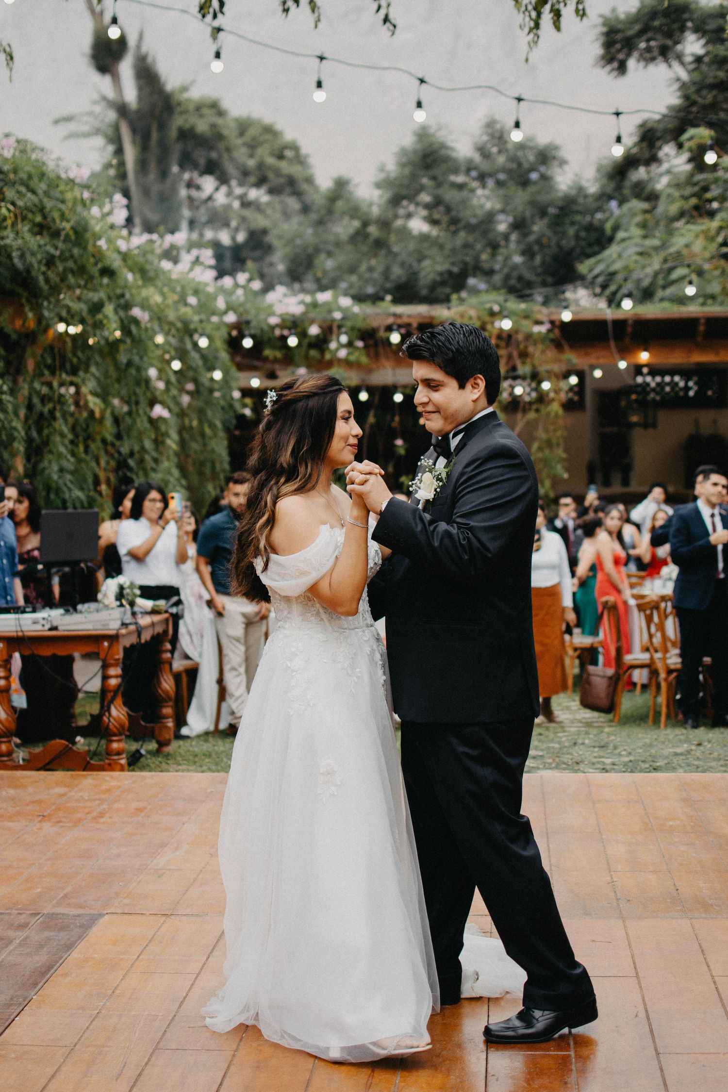 First dance moment at outdoor wedding reception under string lights and greenery.