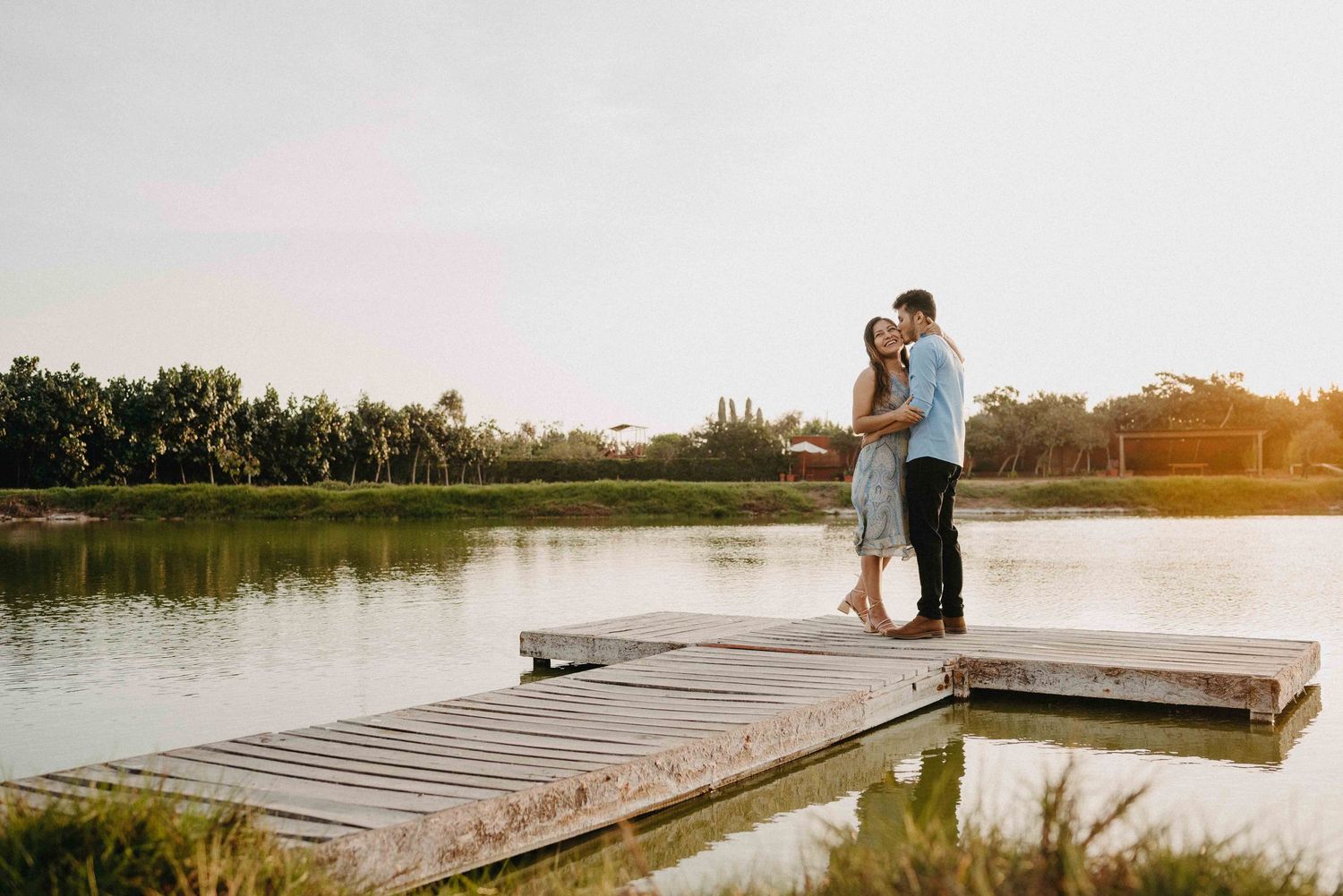 A couple embraces on a wooden dock during sunset over a peaceful lake.