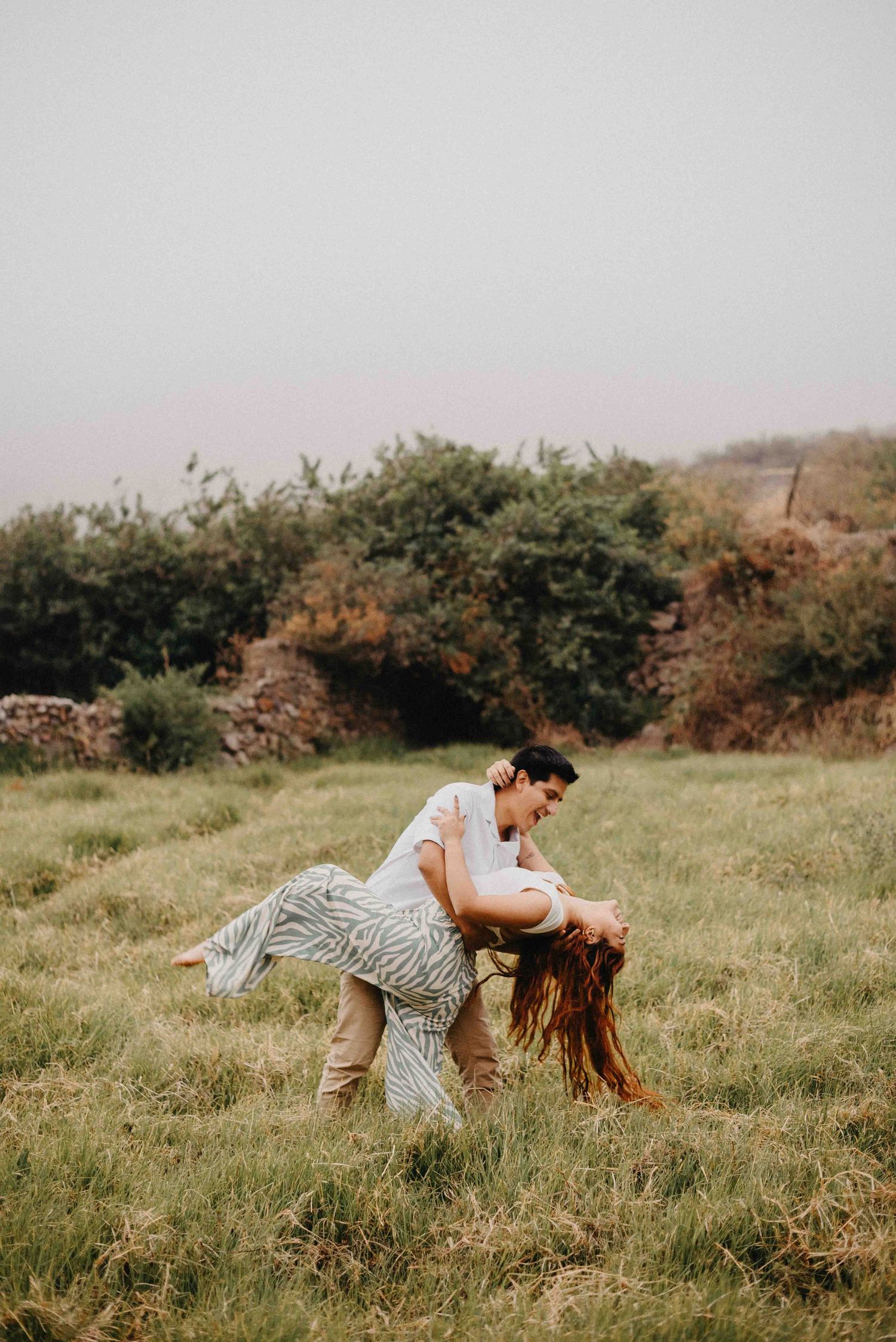Playful couple poses in grassy field during romantic outdoor photoshoot.
