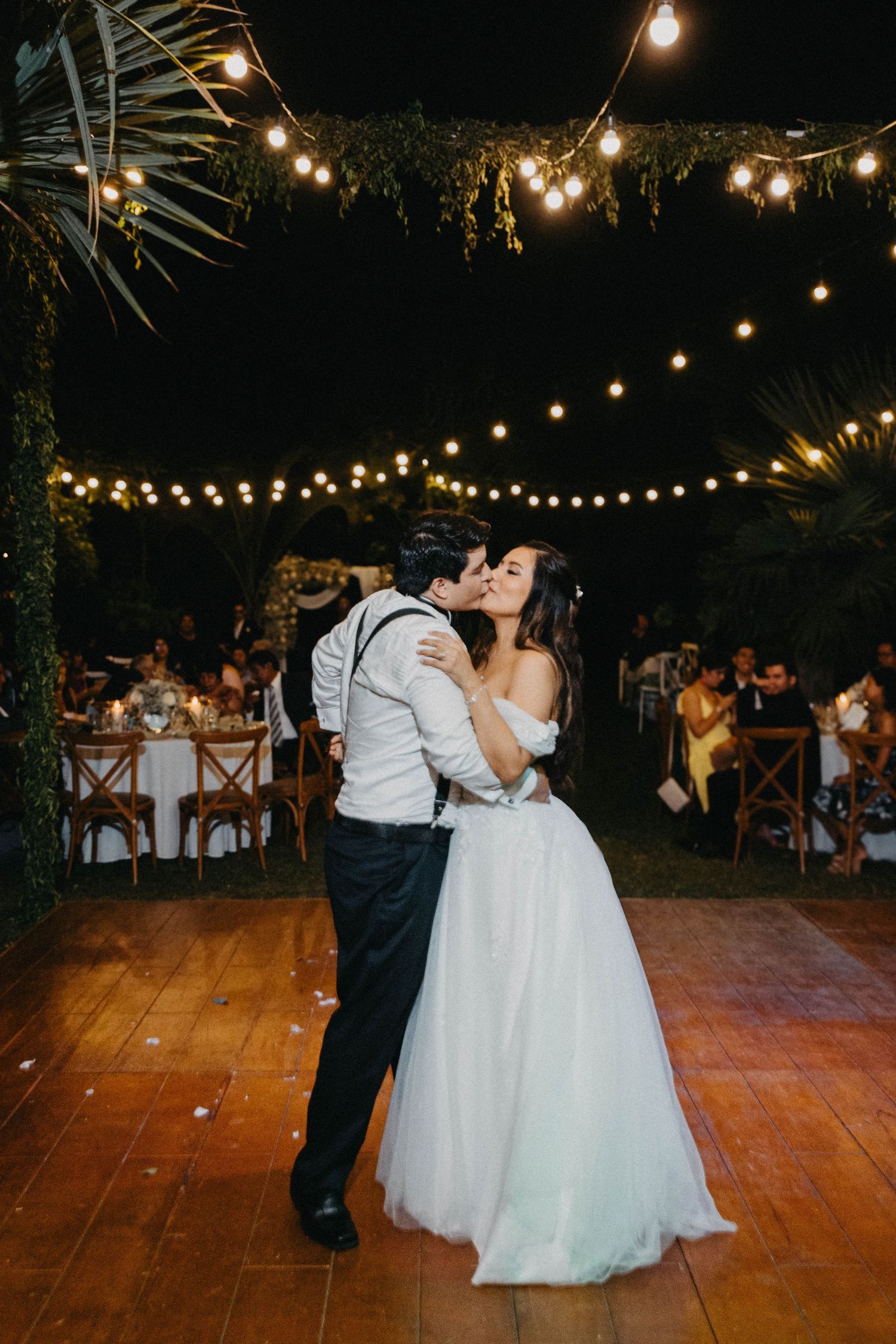 Couple sharing their first dance under string lights at an outdoor wedding reception.