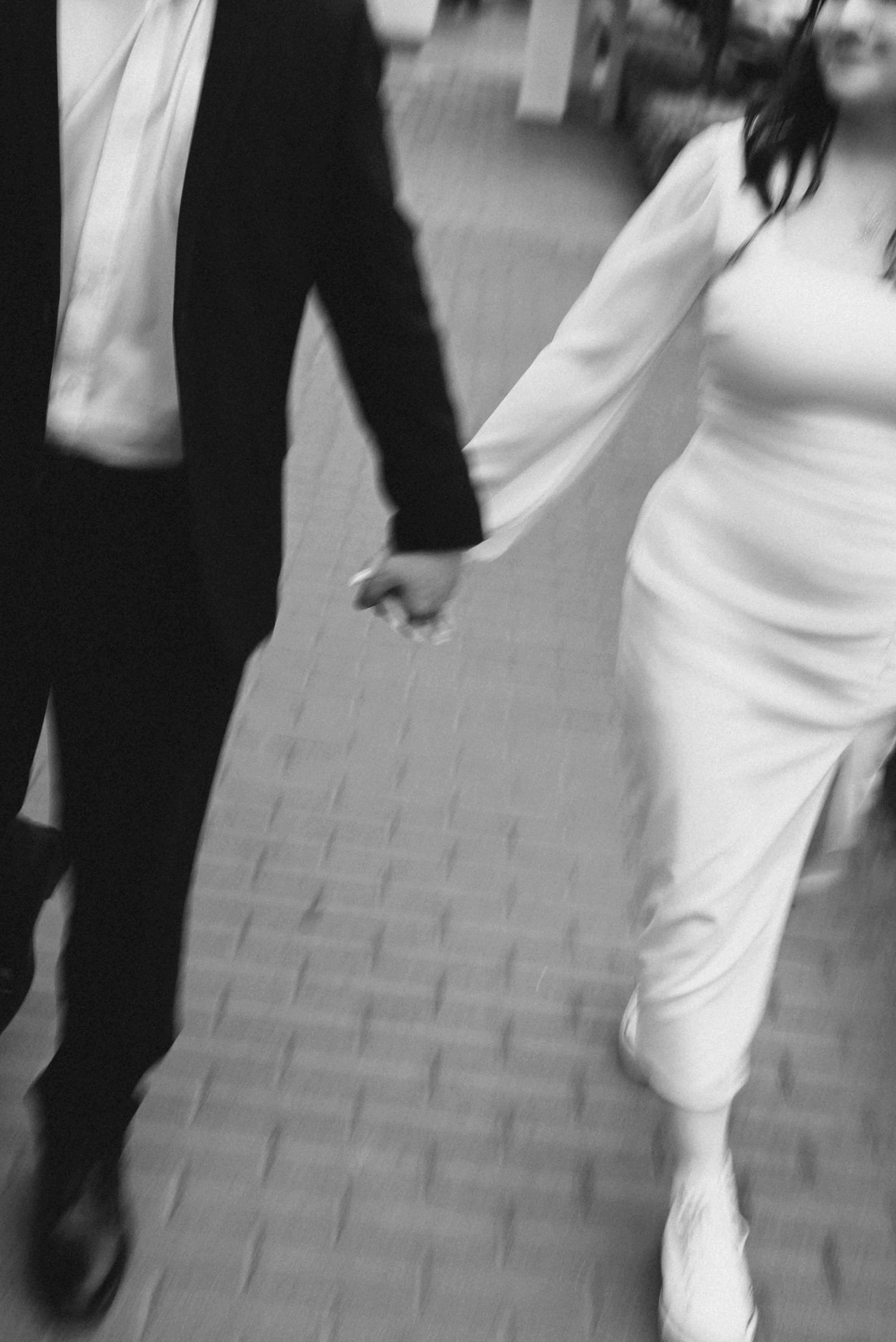 Black and white artistic photo of newlyweds holding hands while walking together.