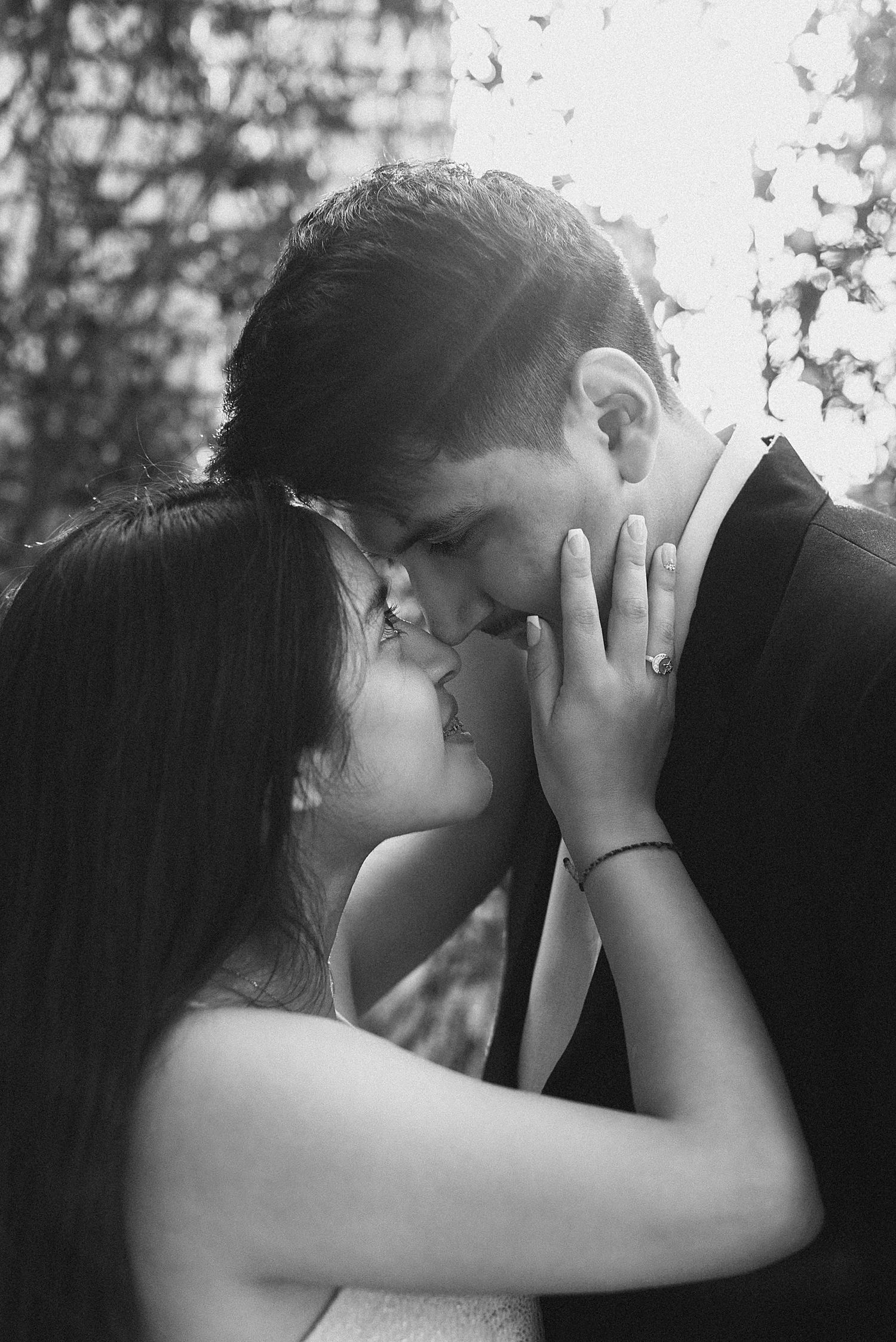 An intimate black and white portrait of a couple sharing a close embrace outdoors.