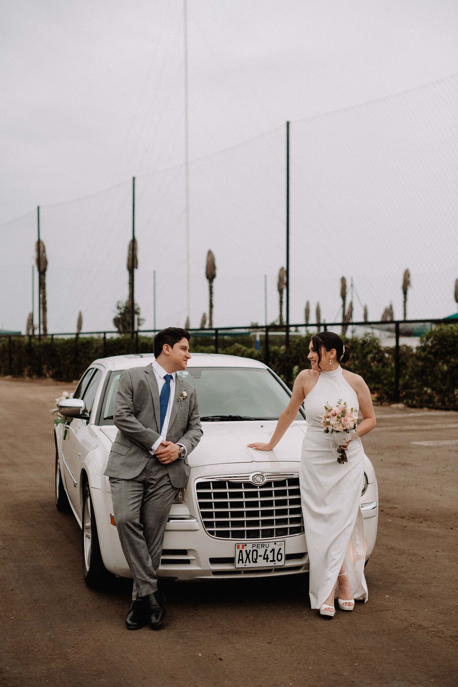 Wedding couple poses elegantly beside white luxury car for formal portraits.