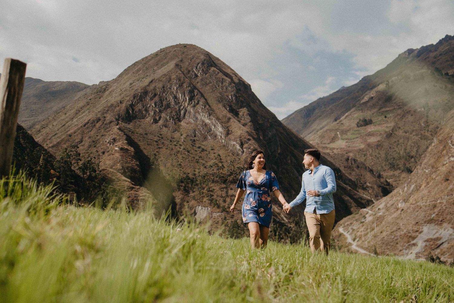 A couple running together through tall grass with dramatic mountain peaks in the background.