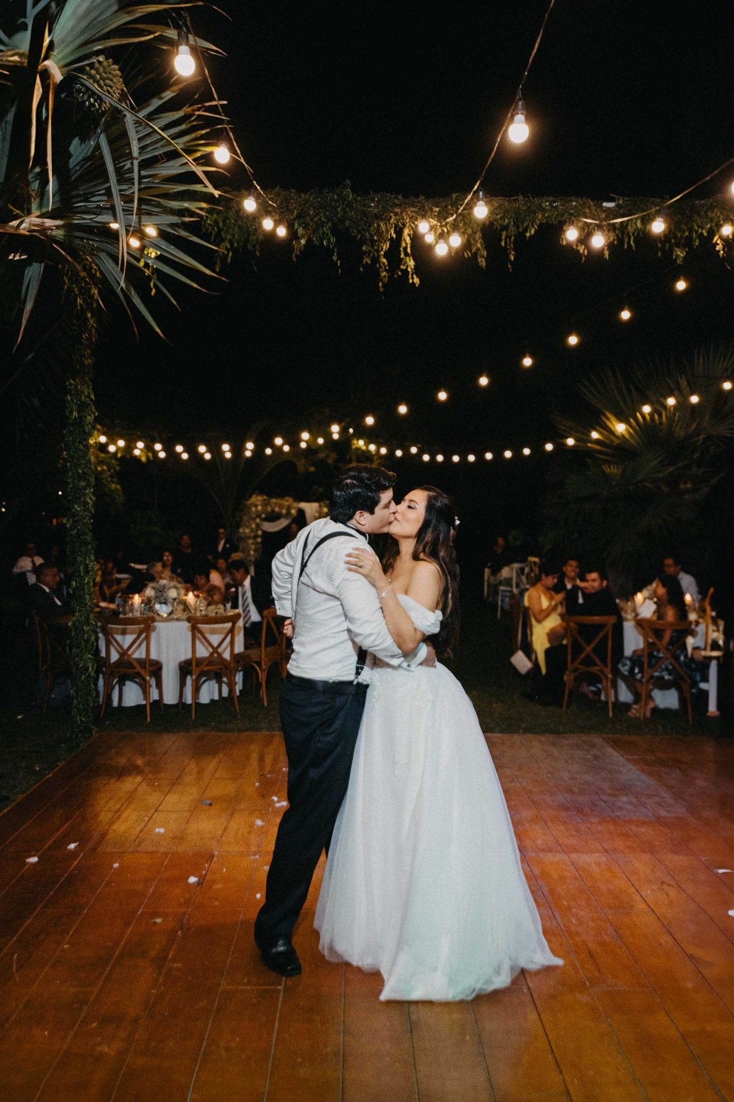 Couple shares a romantic dance under string lights at their outdoor evening reception.
