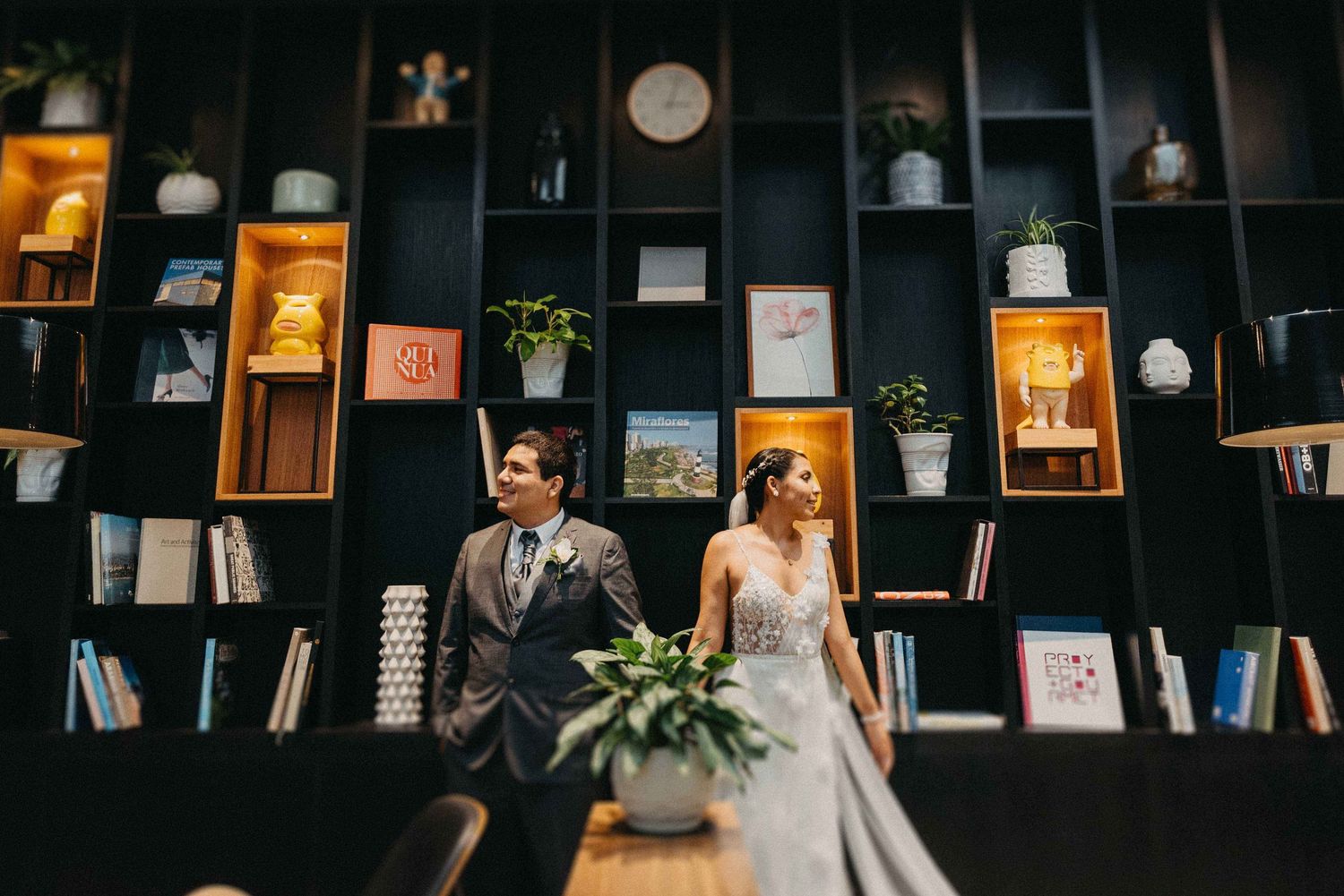 Wedding couple posing against modern bookshelf backdrop in stylish venue.