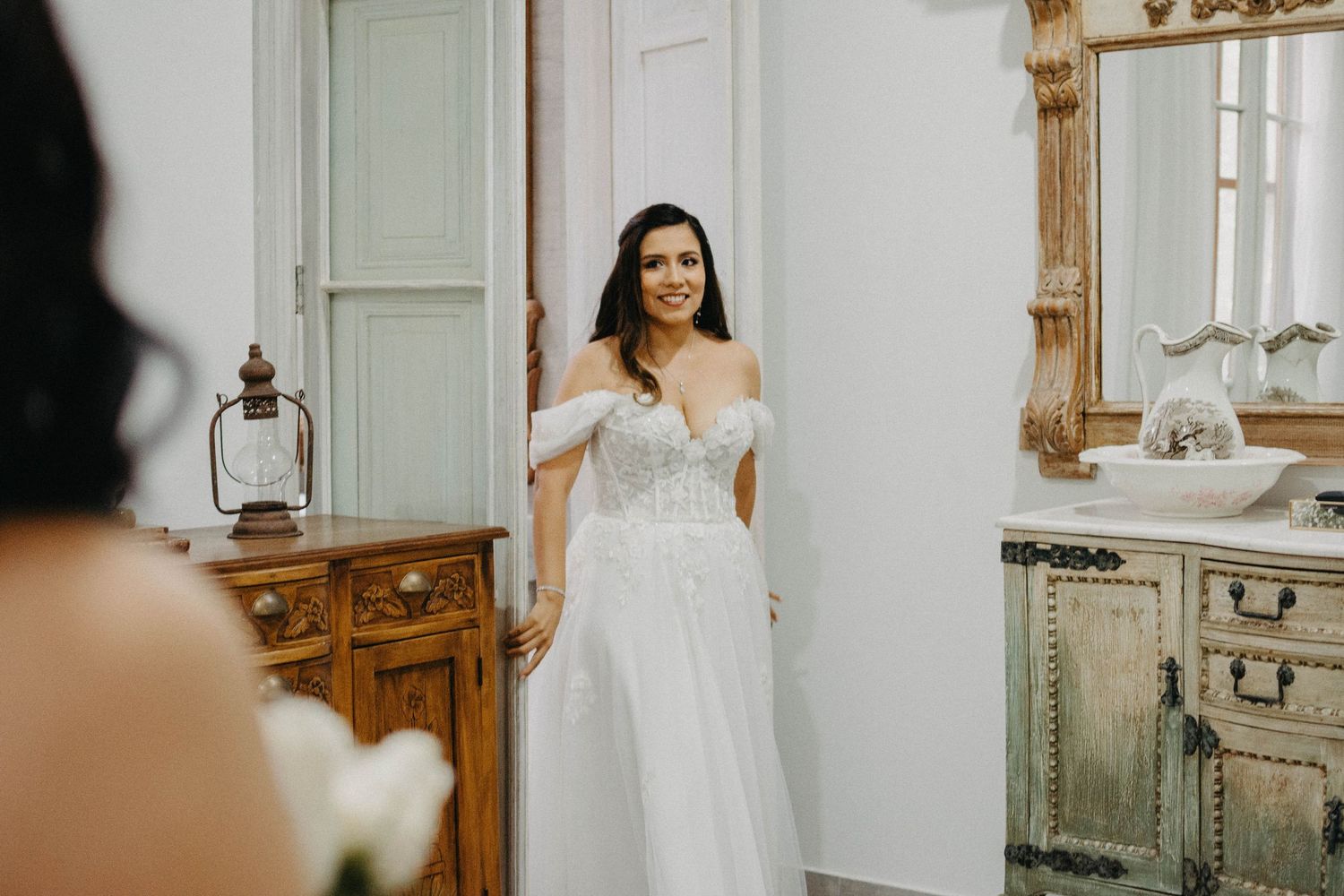 Elegant bridal preparation scene in a bright white room with vintage furniture and natural light.