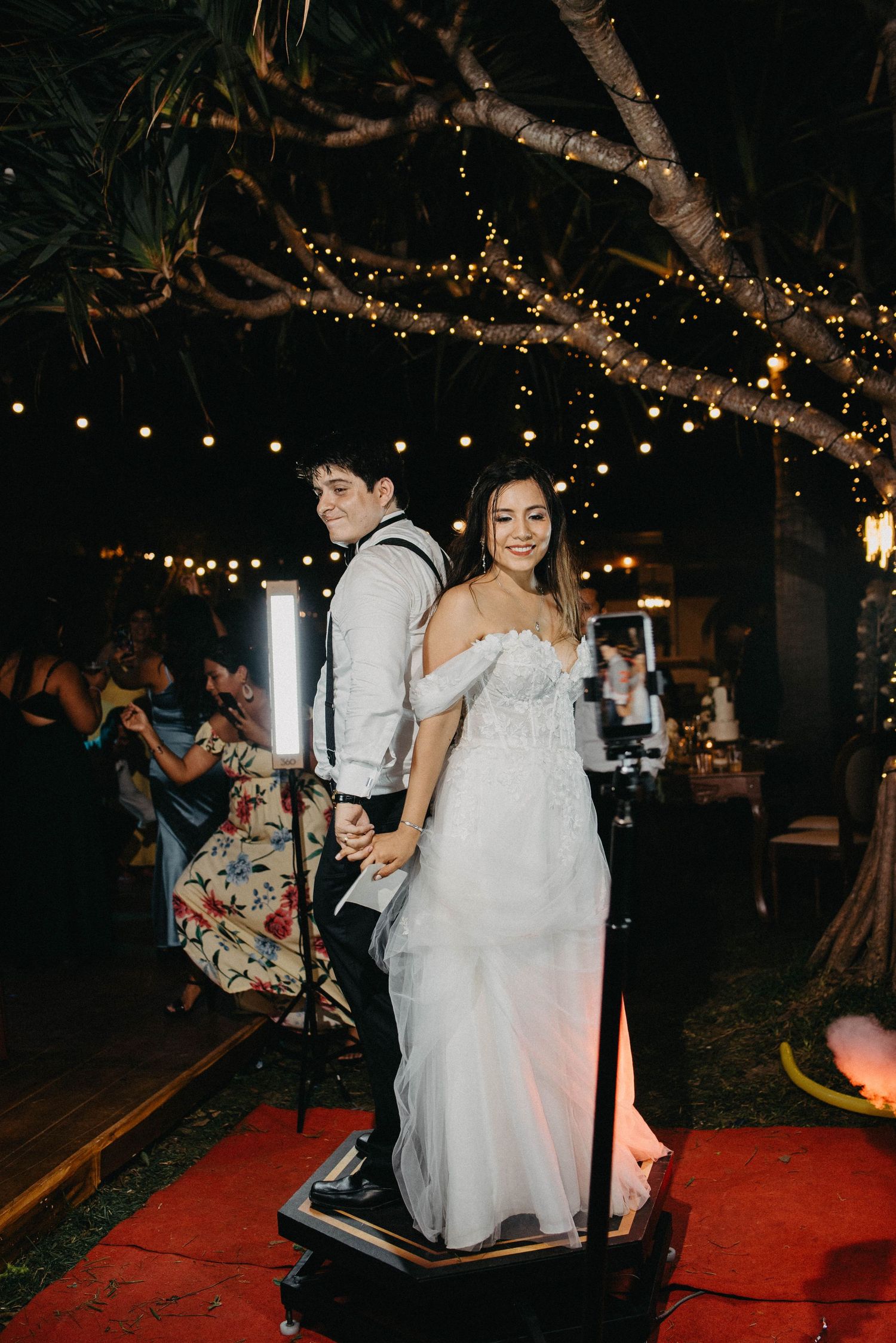 Nighttime wedding reception with string lights and couples dancing on a red carpet dance floor.
