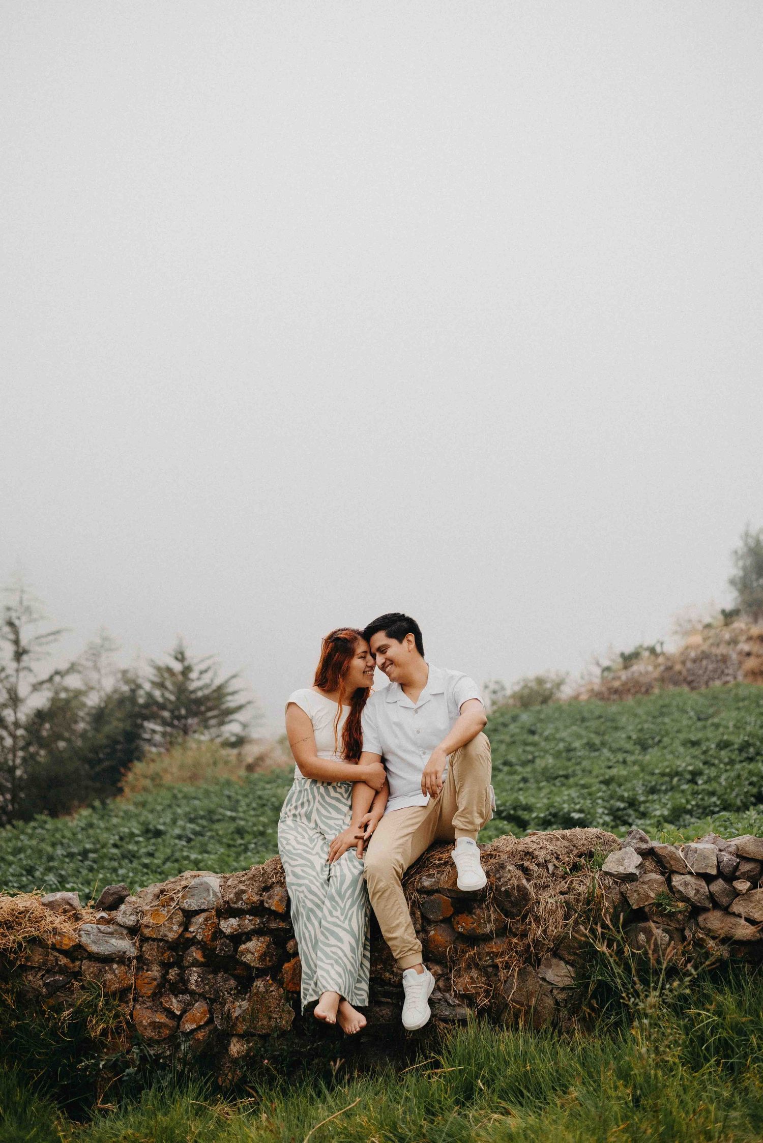 Romantic couple poses together near rustic stone wall during engagement photo session.