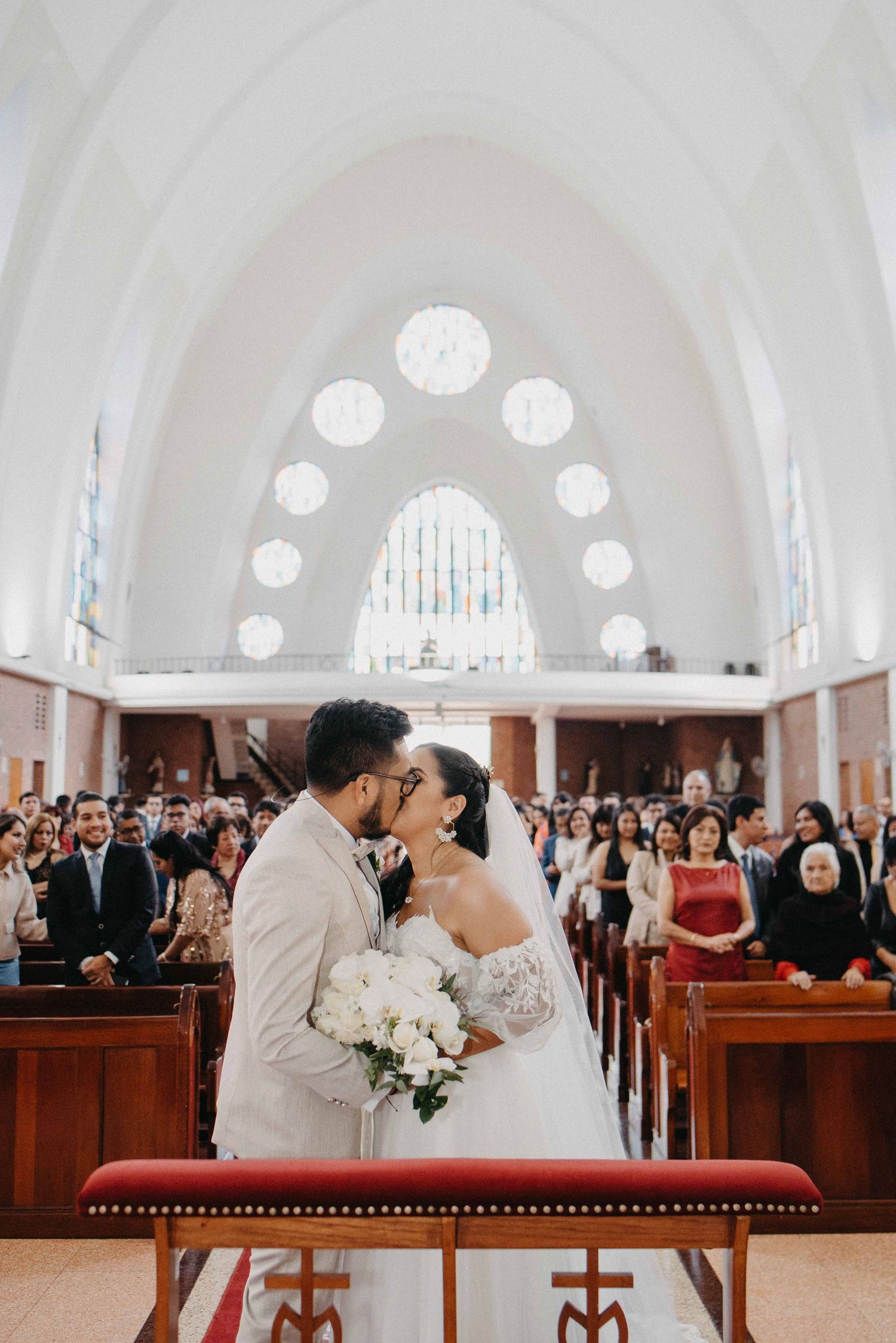 A wedding ceremony in a church with white arched ceilings and stained glass windows.