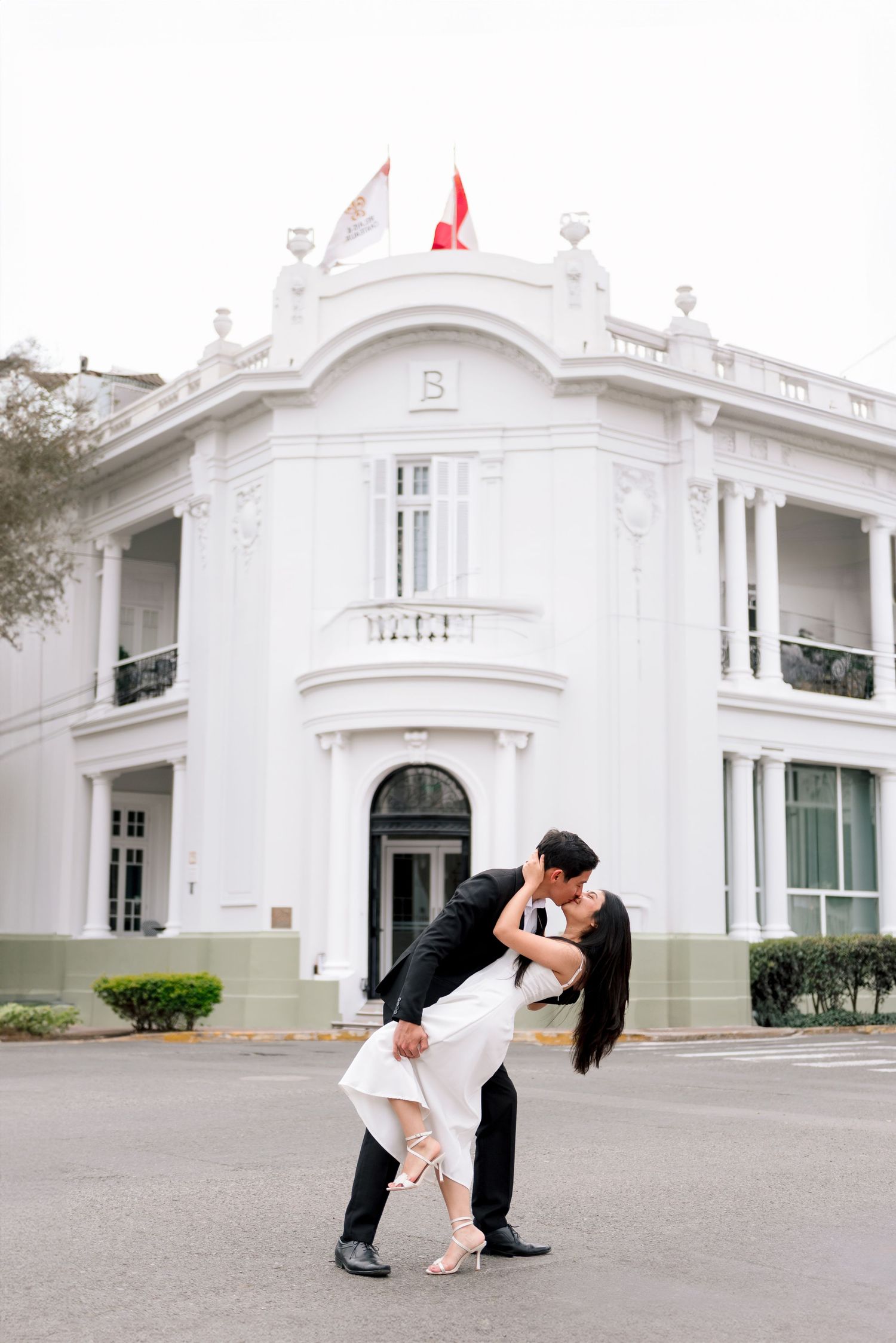 A romantic couple dips in front of an elegant white colonial mansion with ornate architectural details.