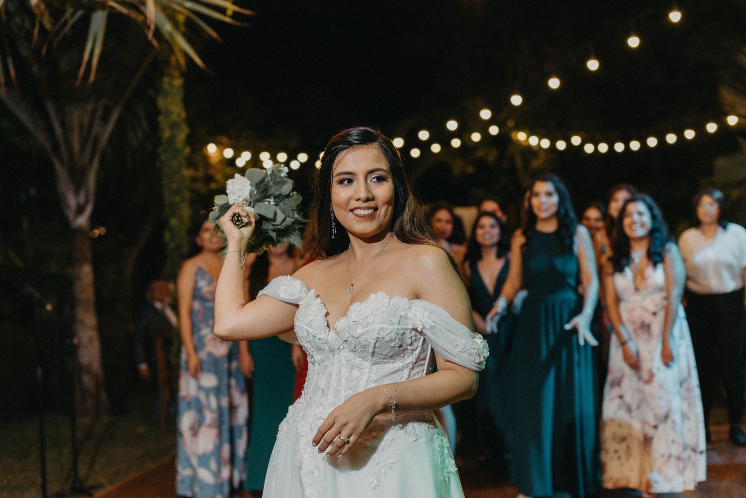 A wedding celebration at night with string lights overhead as guests gather in an outdoor garden setting.