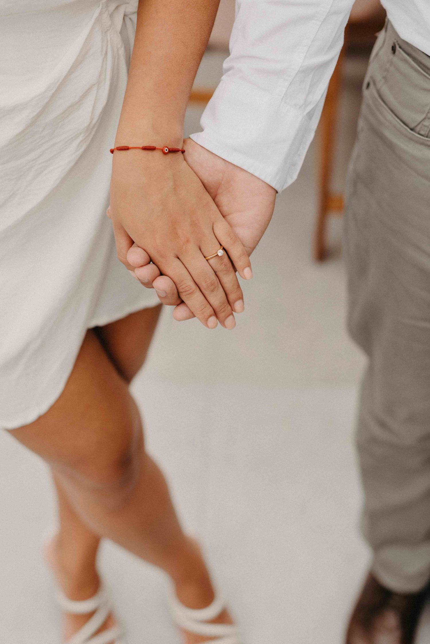 Close-up of newlyweds holding hands showing wedding ring and red string bracelet.