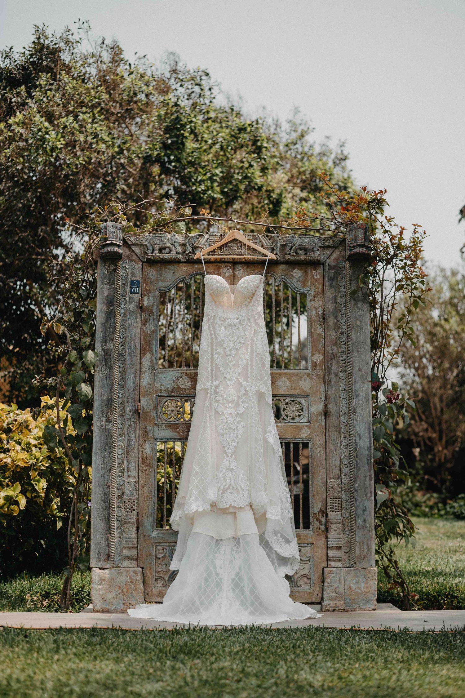Wedding dress displayed on vintage stone archway surrounded by lush greenery.