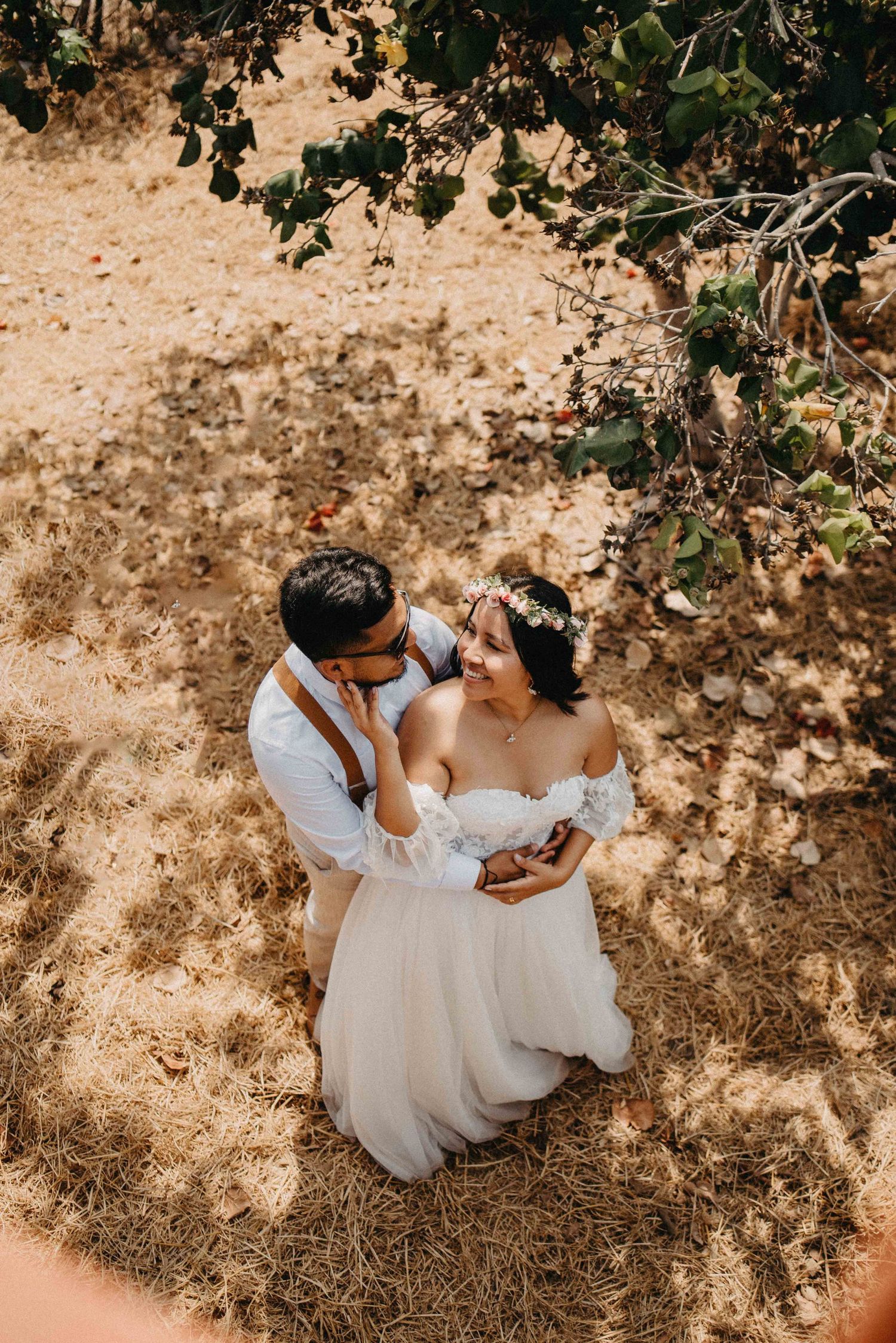 A romantic moment captured from above as a couple embraces in dappled sunlight under trees.
