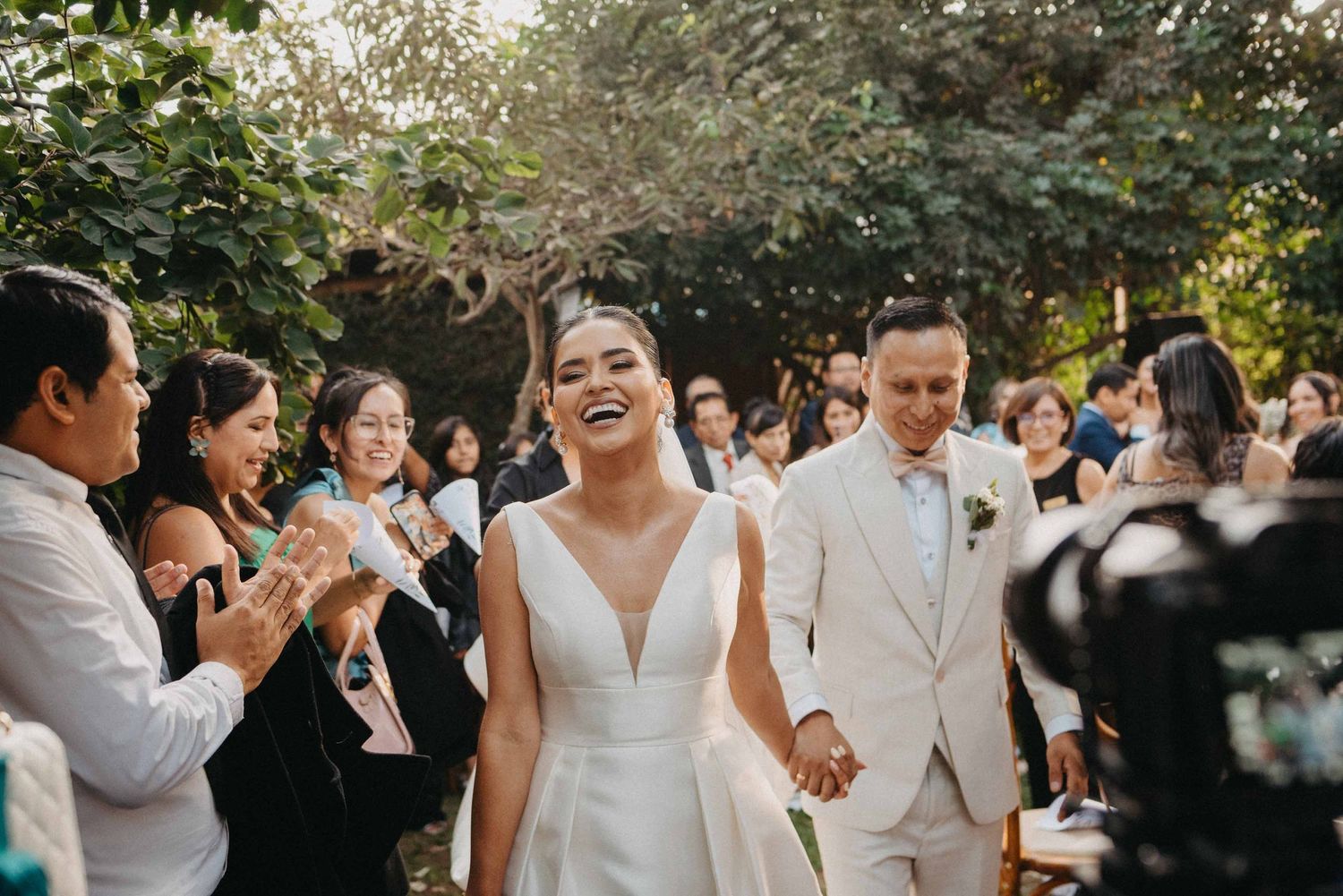 Happy newlyweds walking through cheering guests at outdoor garden wedding ceremony.