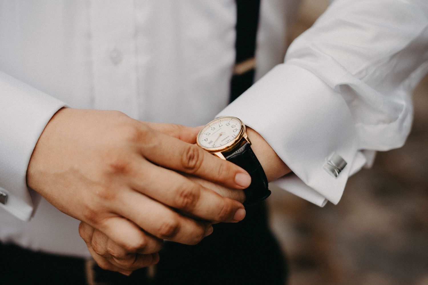 A person checking their wristwatch with a white dress shirt sleeve in close-up detail.