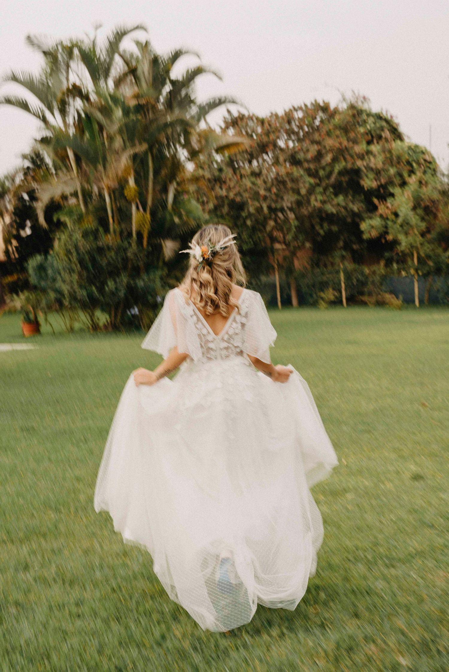 Bride in flowing white dress runs through lush green garden setting.