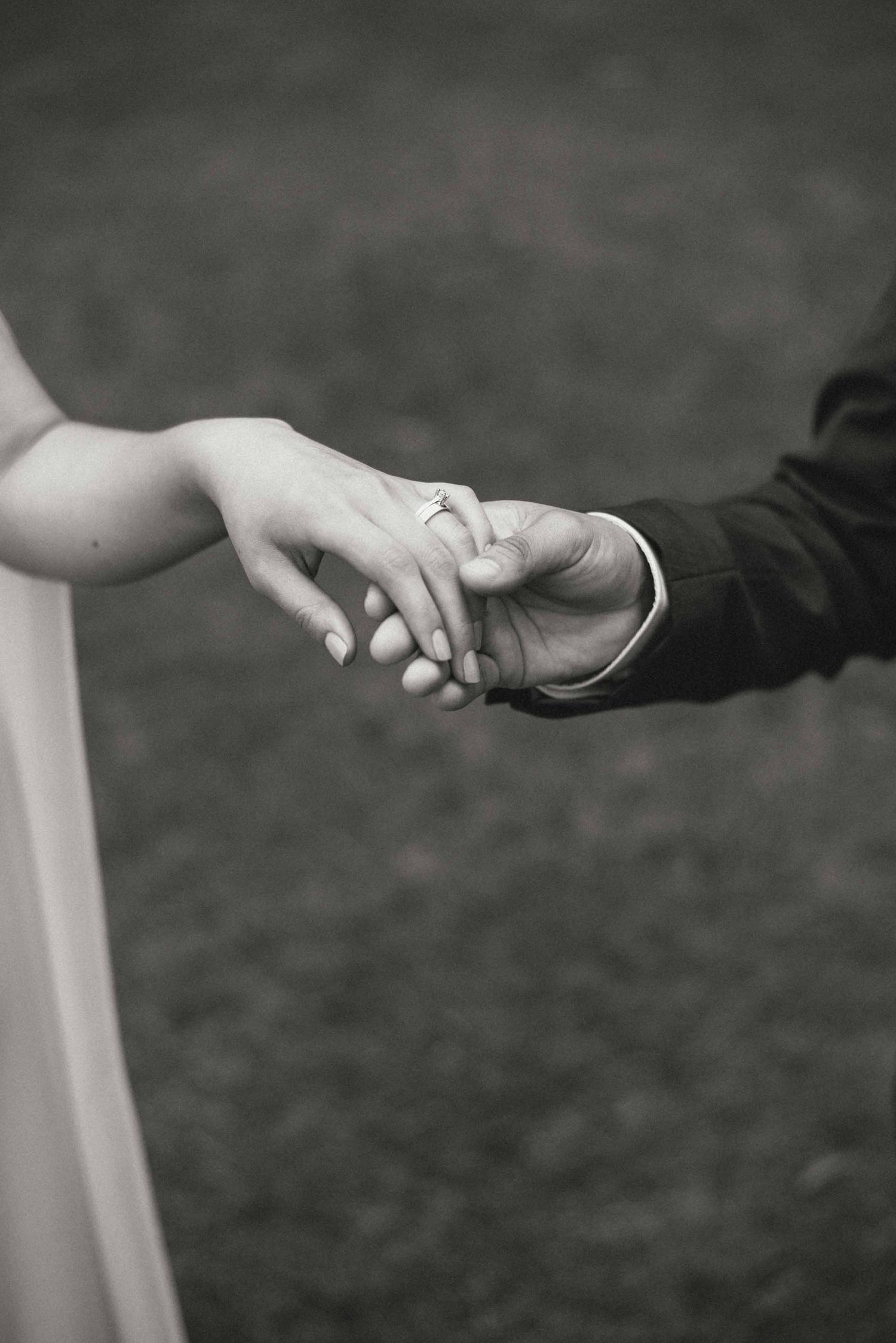 A black and white close-up of newlyweds holding hands, showing the wedding ring.