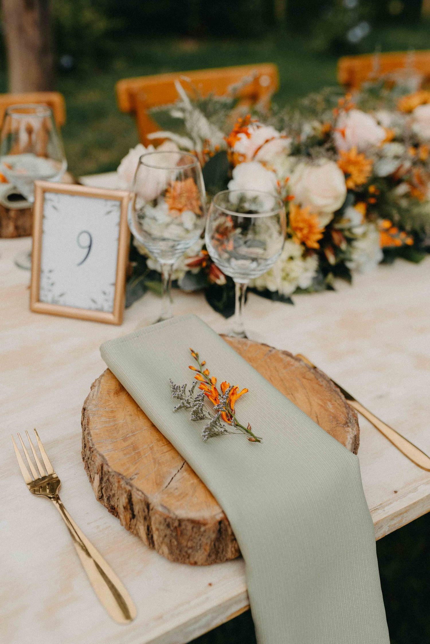Rustic wedding table setting with wood slice charger, table number and orange floral centerpiece.