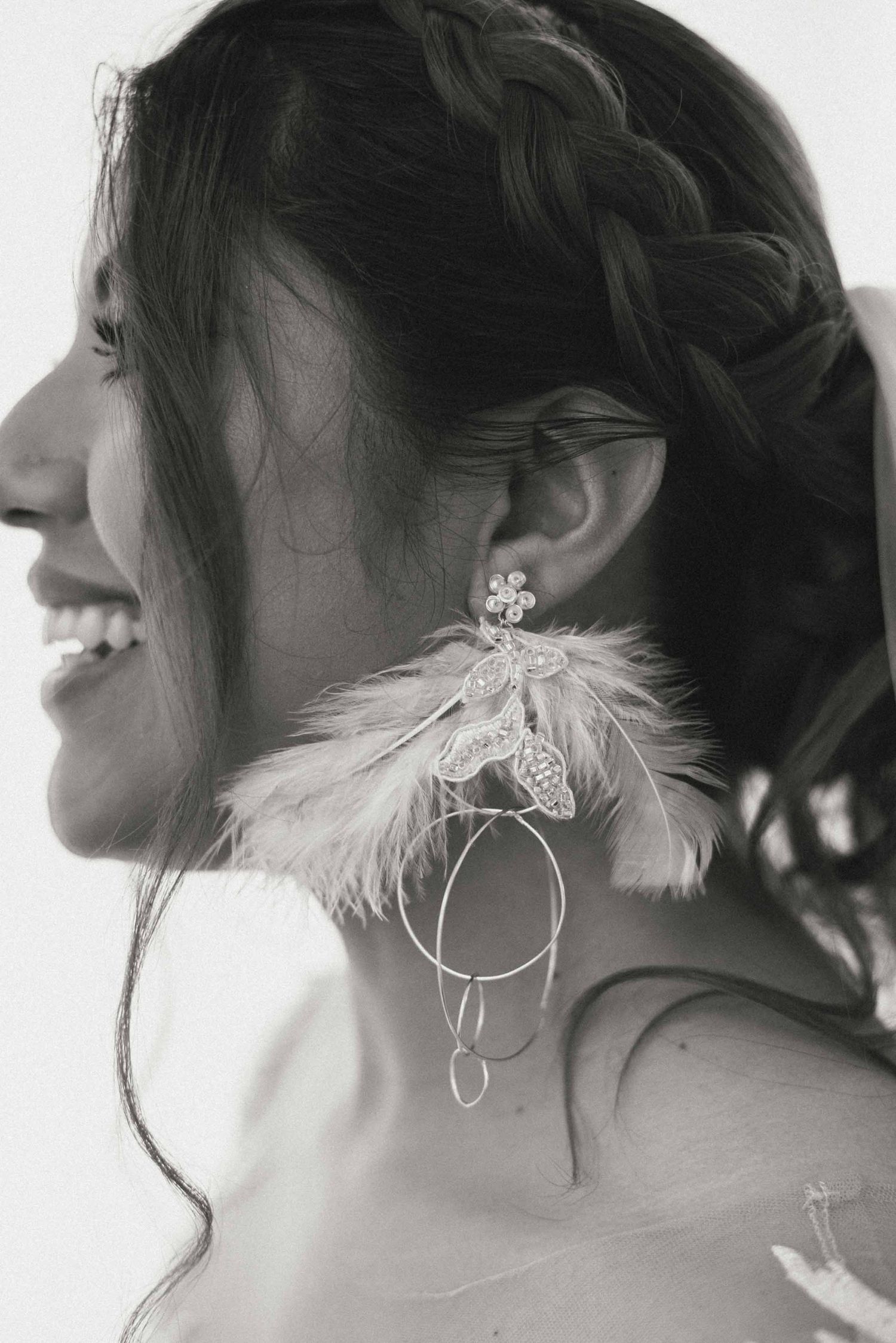 A black and white profile shot of a bride wearing an elegant feathered statement earring.