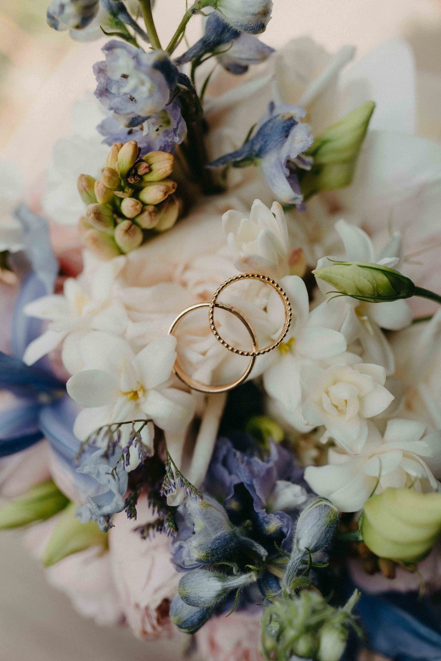 Delicate wedding rings nestled among white and blue flower bouquet arrangements.