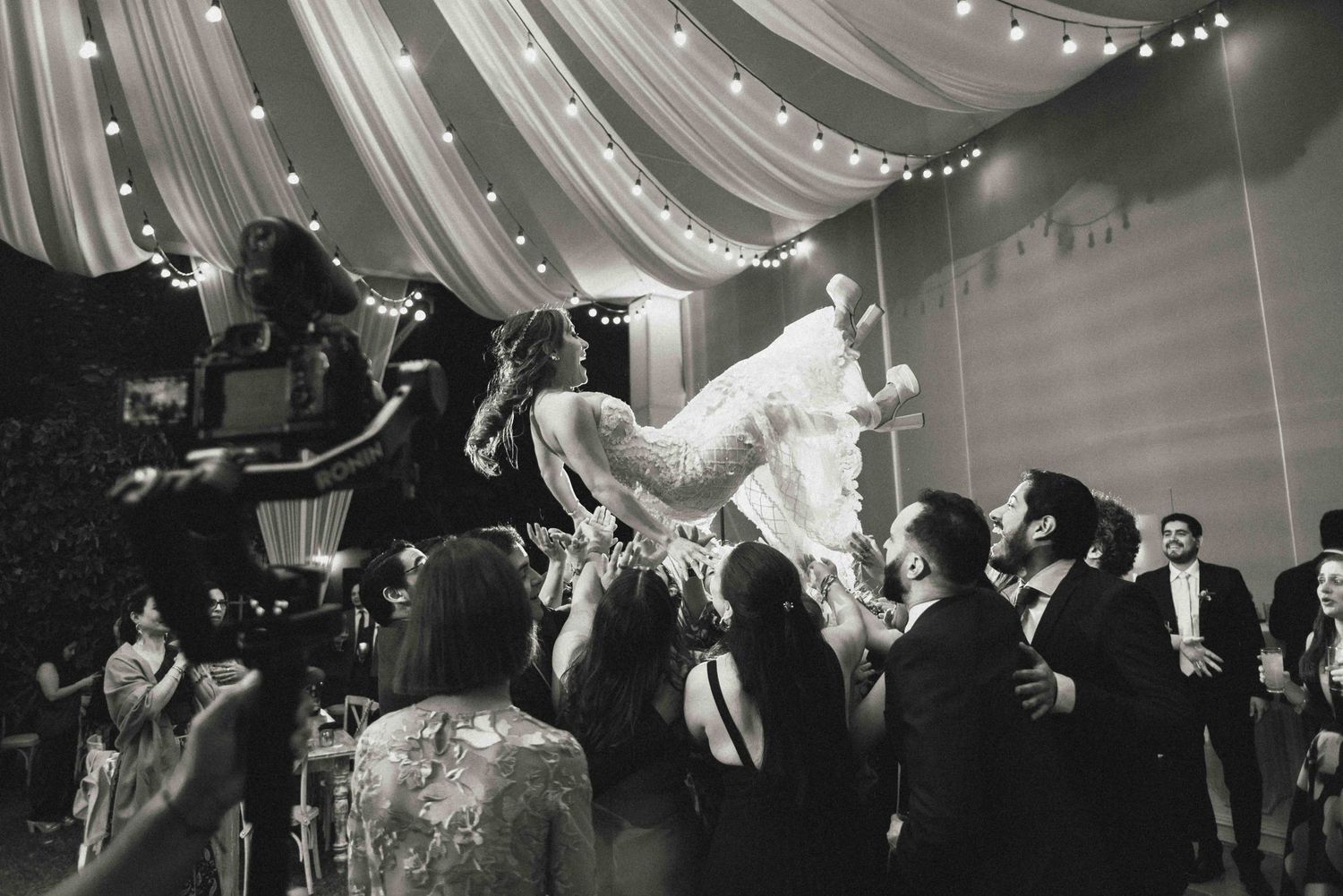 Wedding guests lift and hold the newlyweds up during a lively reception celebration.