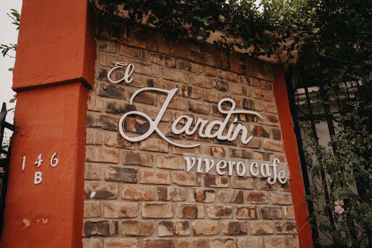 Rustic brick wall with vintage metal house numbers and handwritten script signage in terracotta tones.