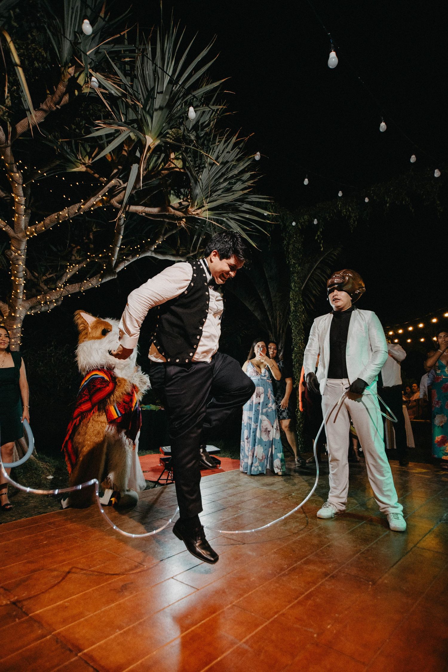 Wedding guests dancing on an outdoor wooden dance floor under string lights.