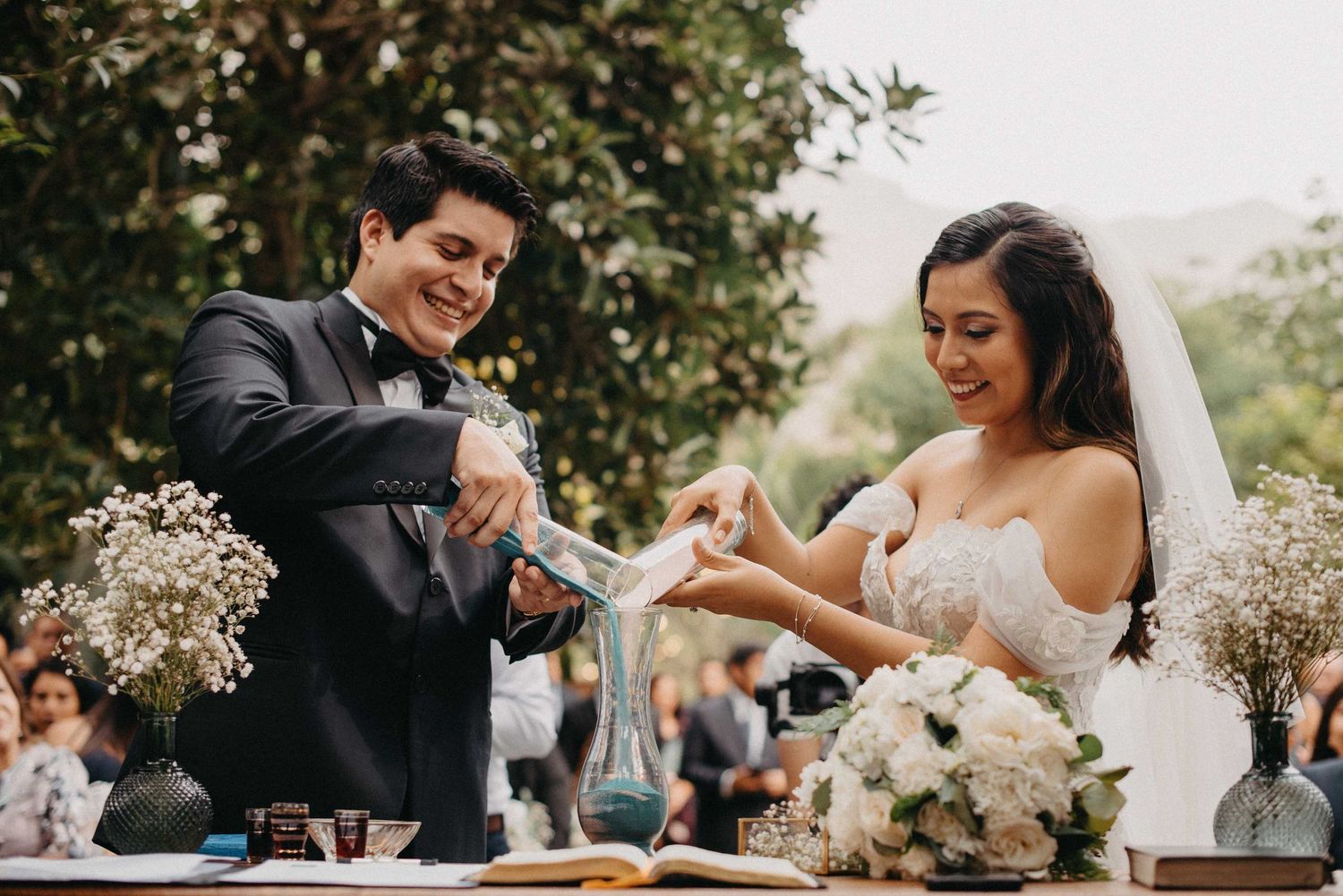 A couple laughs while performing their unity ritual during their outdoor garden wedding ceremony.